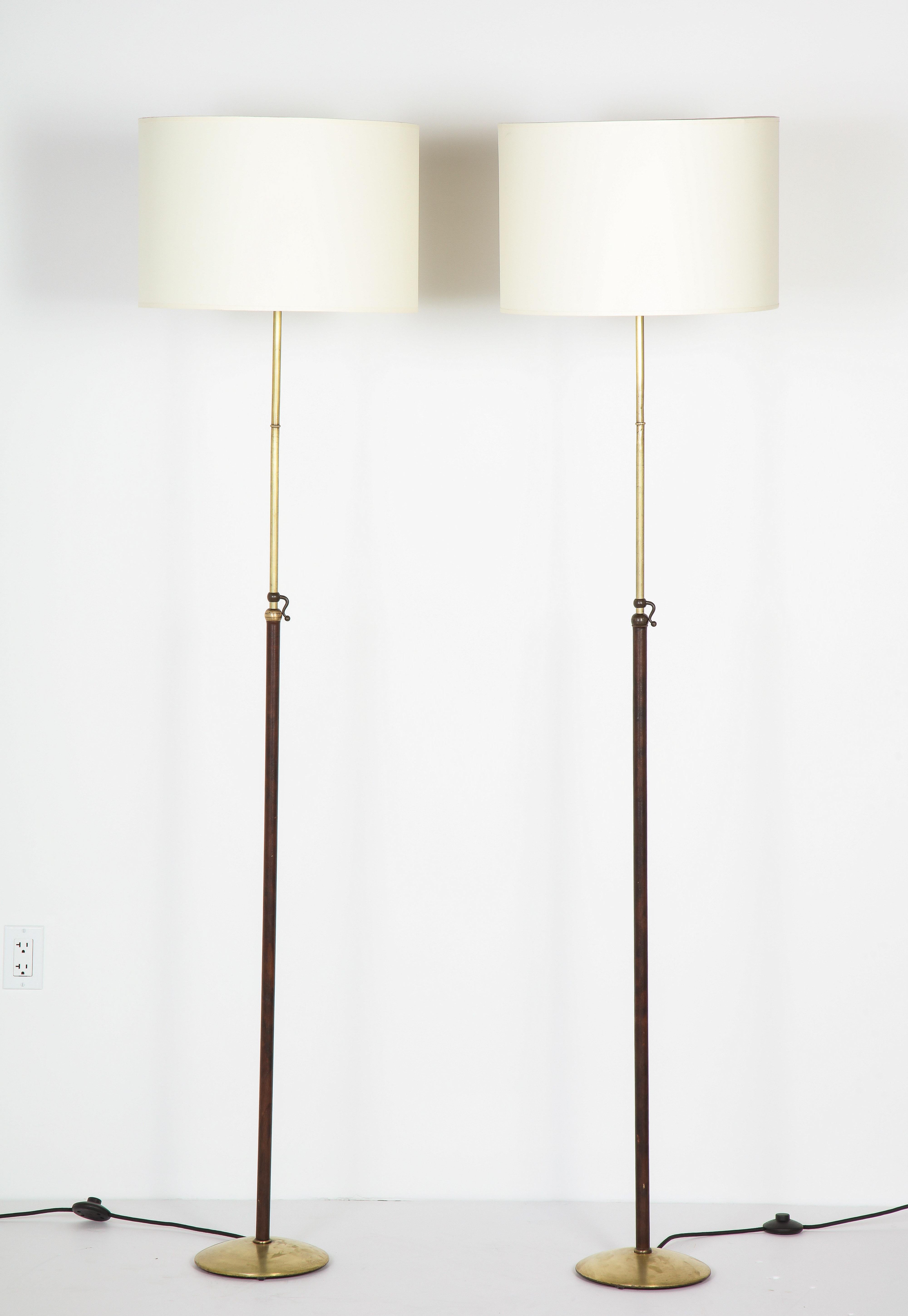 Pair of leather and brass adjustable floor lamps by Jacques Adnet, leather is original, brass has been lightly restored. Rewired. Base is 10'' in diameter, extends to 75''.