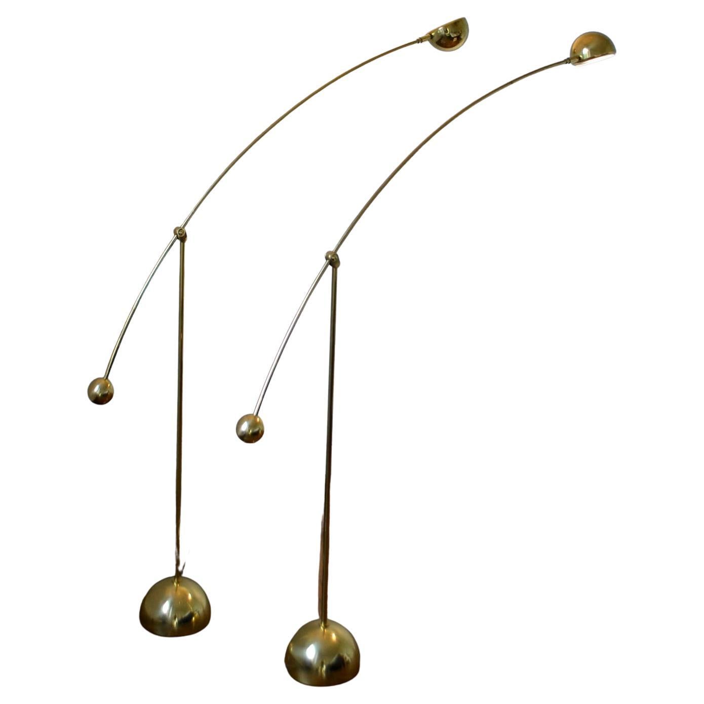 A pair of brass floor lamps is attached to a long bowed arm holding a spherical bronze light source that is adjustable by a up and down movement from the vertical stand. The light source can be pivoted in a 180 degrees direction as needed; this