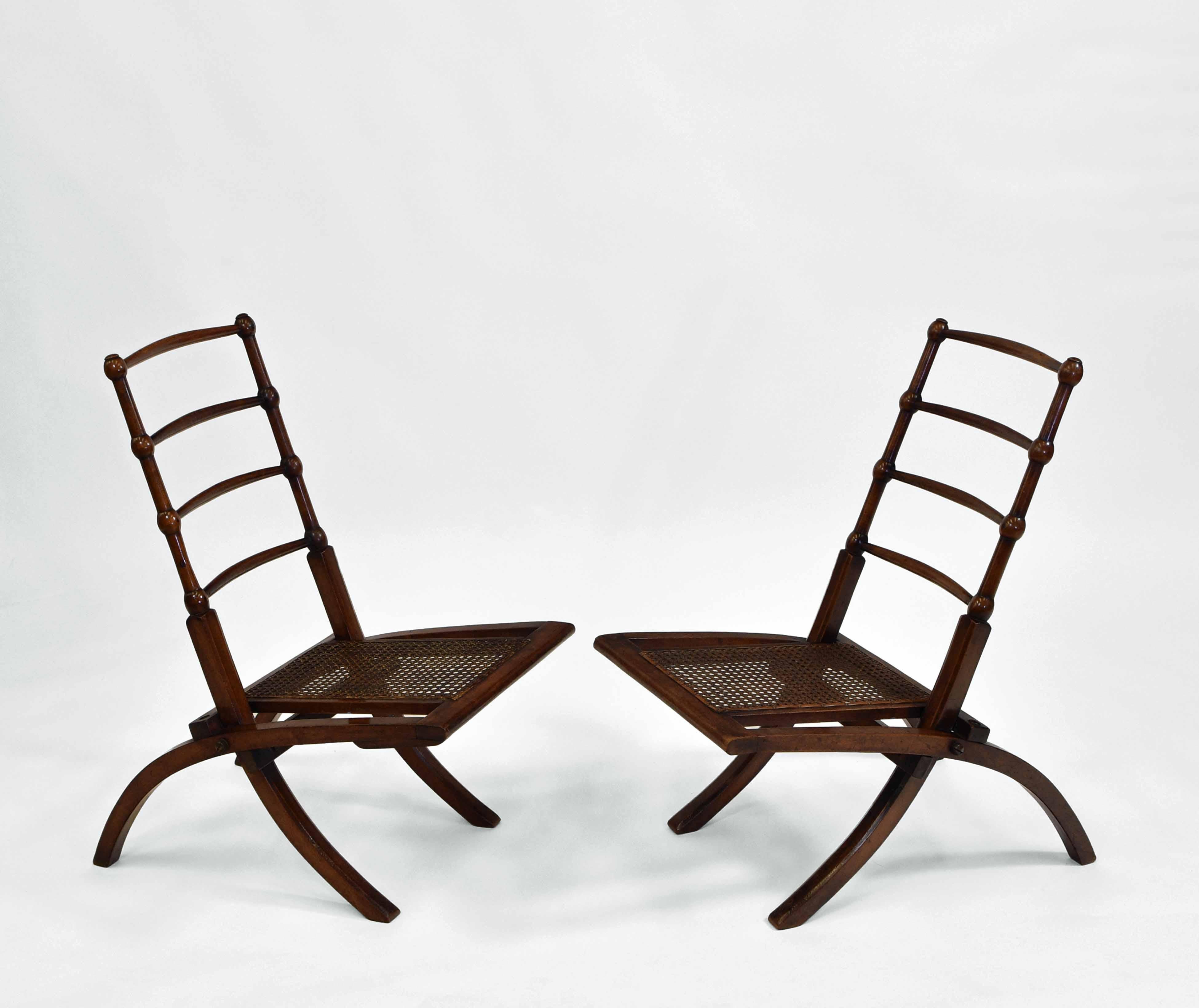 A pair of Aesthetic Movement small walnut low folding decorative chairs with cane seats, in the manner of E.W. Godwin. Circa 1870s.

Free delivery to the UK via a selected parcel company.

The walnut frames are in very good condition and have