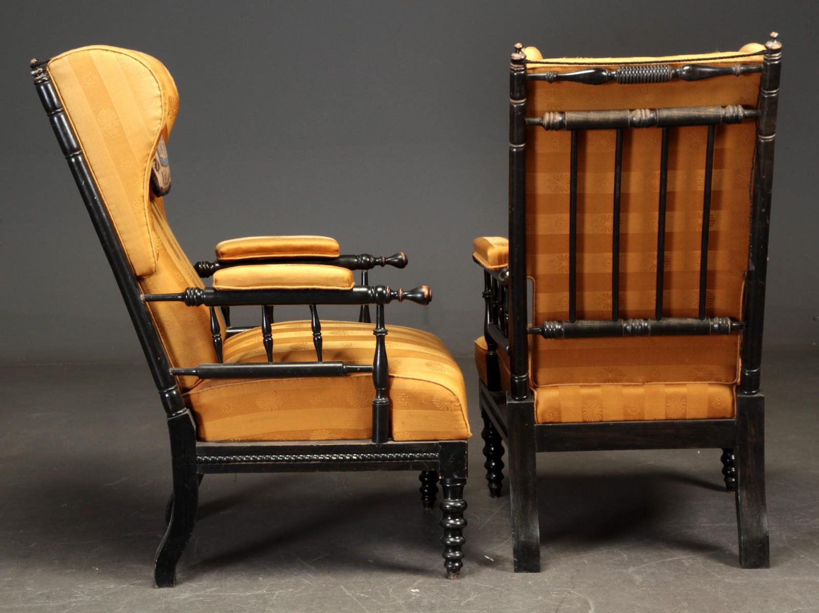 Pair of aesthetic period wingback armchairs. Black painted wooden frame, carved back splats lightly decorated, late 19th century. Upholstered in striped yellow fabric. A petit-point headrest accompanies each chair.