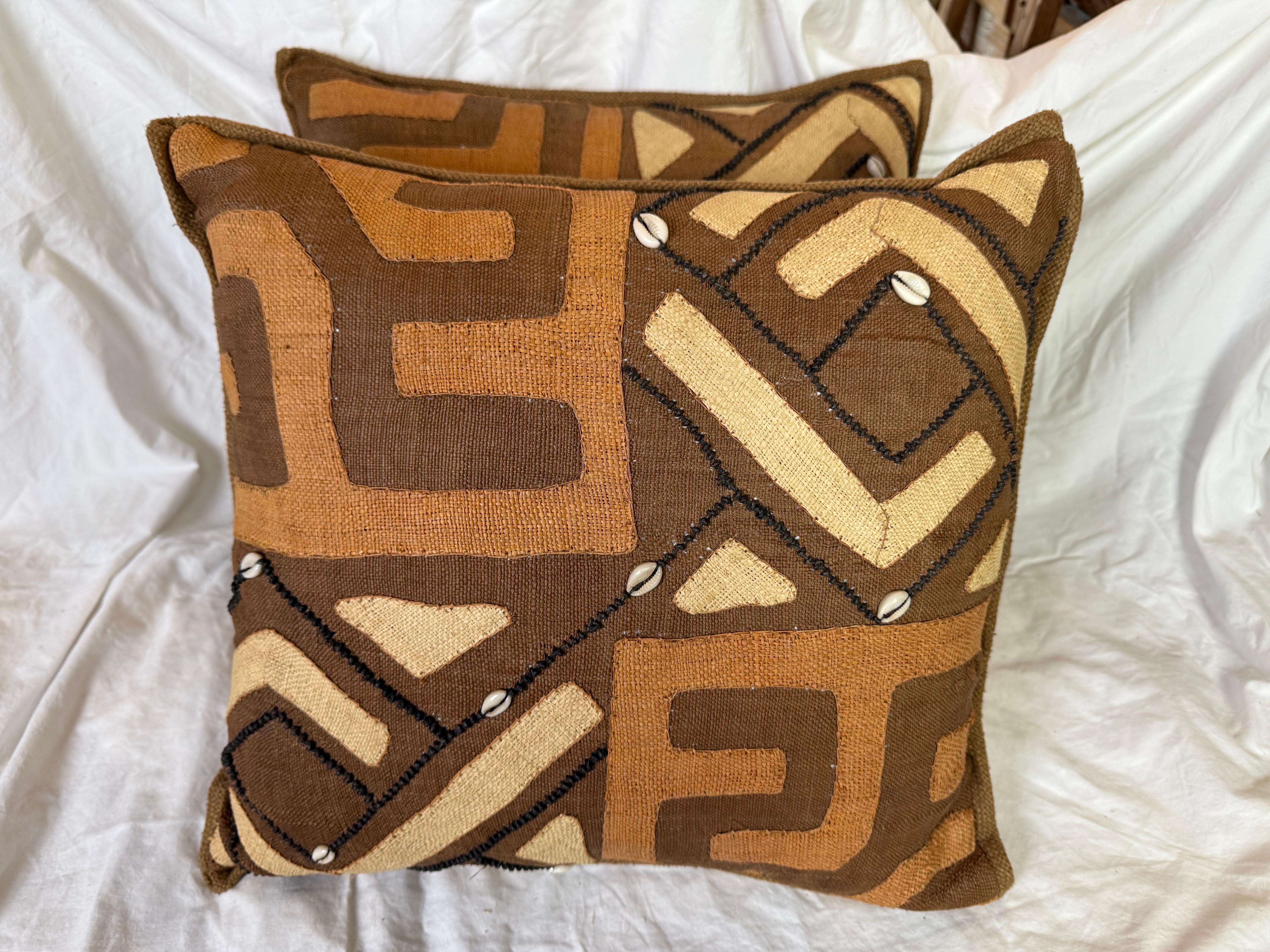 Questi cuscini vintage in tessuto Kuba sono ricchi di consistenza, storia e significato culturale. Realizzati a mano con l'autentico tessuto africano Kuba, presentano audaci motivi geometrici nei toni della terra del marrone, del marrone e del nero,