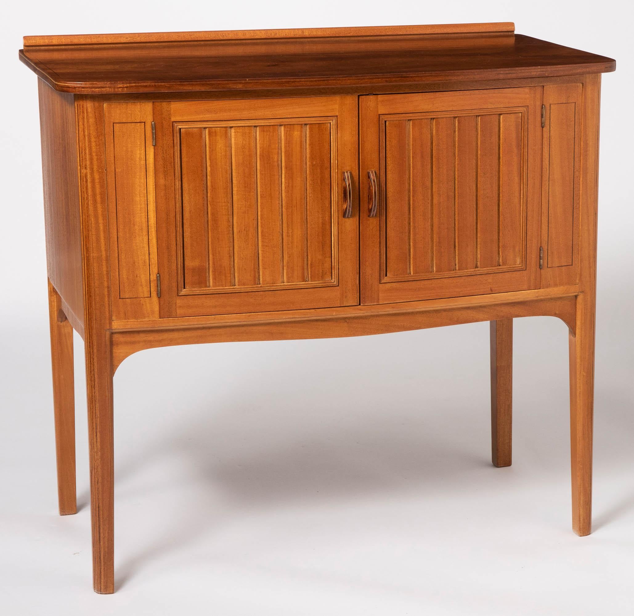 Pair of side cabinets by Edward Barnsley C.B.E
African mahogany with holly-wood stringing.
The rectangular tops with rounded corners above a pair of shuttered panel doors with moulded handles.
Holly stringing.
Shaped apron above moulded square