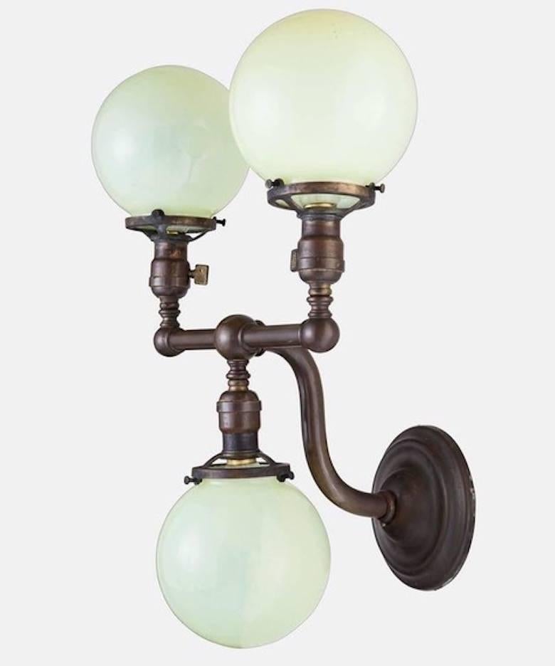 An elegant pair of brass scones with Vaseline glass globes, circa 1920s. Globes are six inches in diameter, hand blown, light green, slightly opaque. Brass fittings with three sockets. Brass has a rich patina.