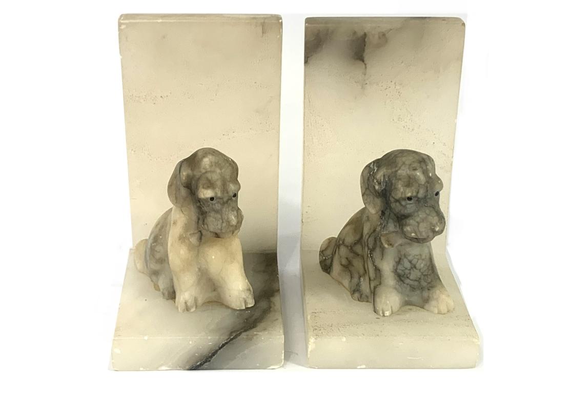 Paar Alabaster-Buchstützen mit je einem sitzenden Hund. Der halbtransparente Stein ist mit dunklen Adern durchzogen.

Abmessungen: 2 5/8