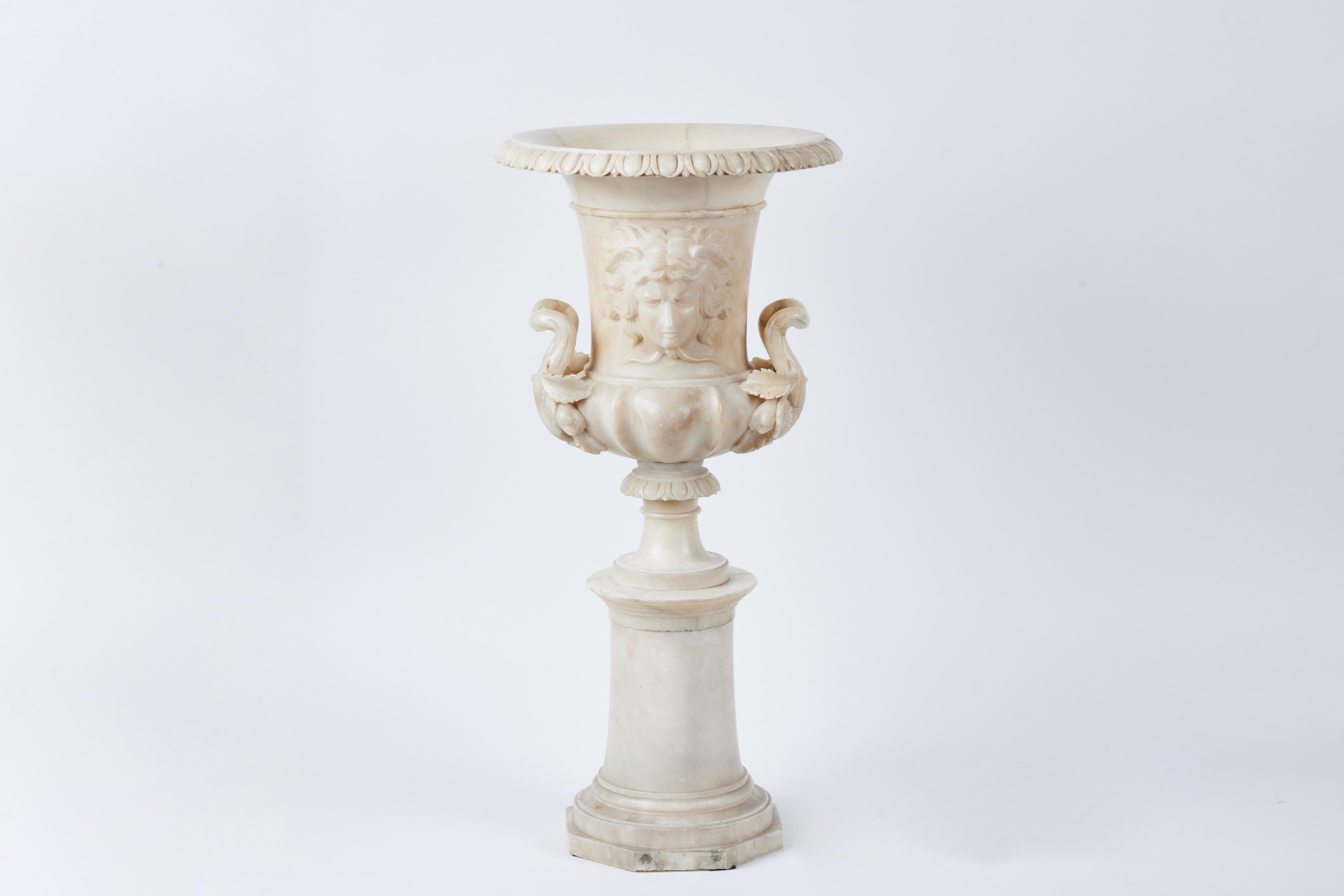A striking pair of hand carved alabaster urns featuring the face of Mercury, sinuous foliate arms, rims of acanthus leaves, on a stepped base.  