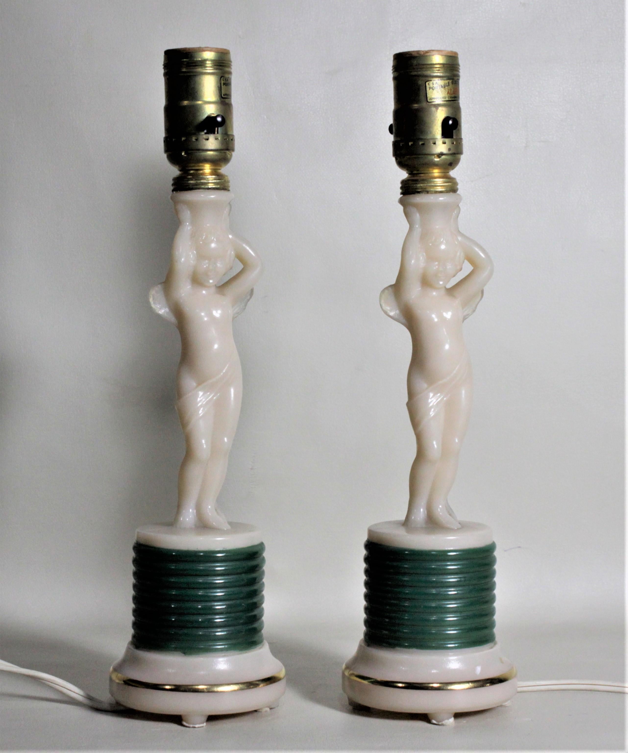 This pair of Art Deco figural winged cherub table lamp bases were produced by the Aladdin Company of the United States in circa 1935. The lamps are done in an alabaster toned glass or alacite and molded into sculptural cherubs on pedestal bases. The