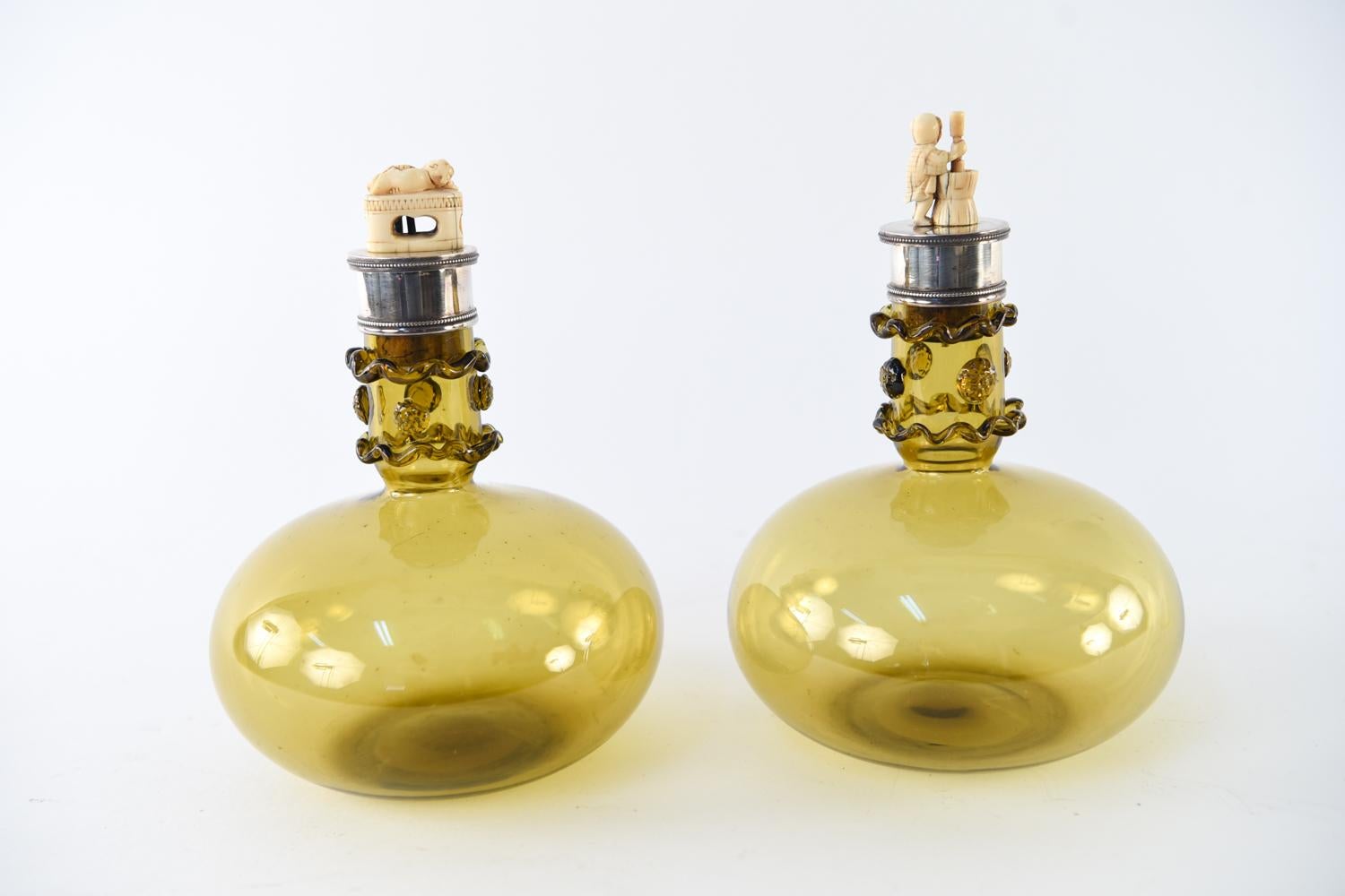 This spectacular pair of decanters dates to the Aesthetic Movement in Victorian England, circa 1886. Their amber glass bodies feature hand-applied decoration at the neck and beaded sterling silver collars. Each sterling and cork stopper is topped