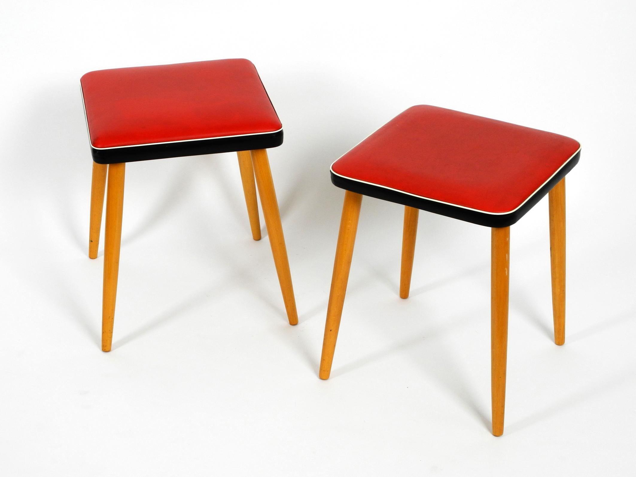 Pair of very nice four-legged wooden stools with red faux leather. Almost new condition. 
Probably never used and barely no traces of wear, light traces of storage.
The seats are very clean and without damages. No cracks. 
The clear lacquered