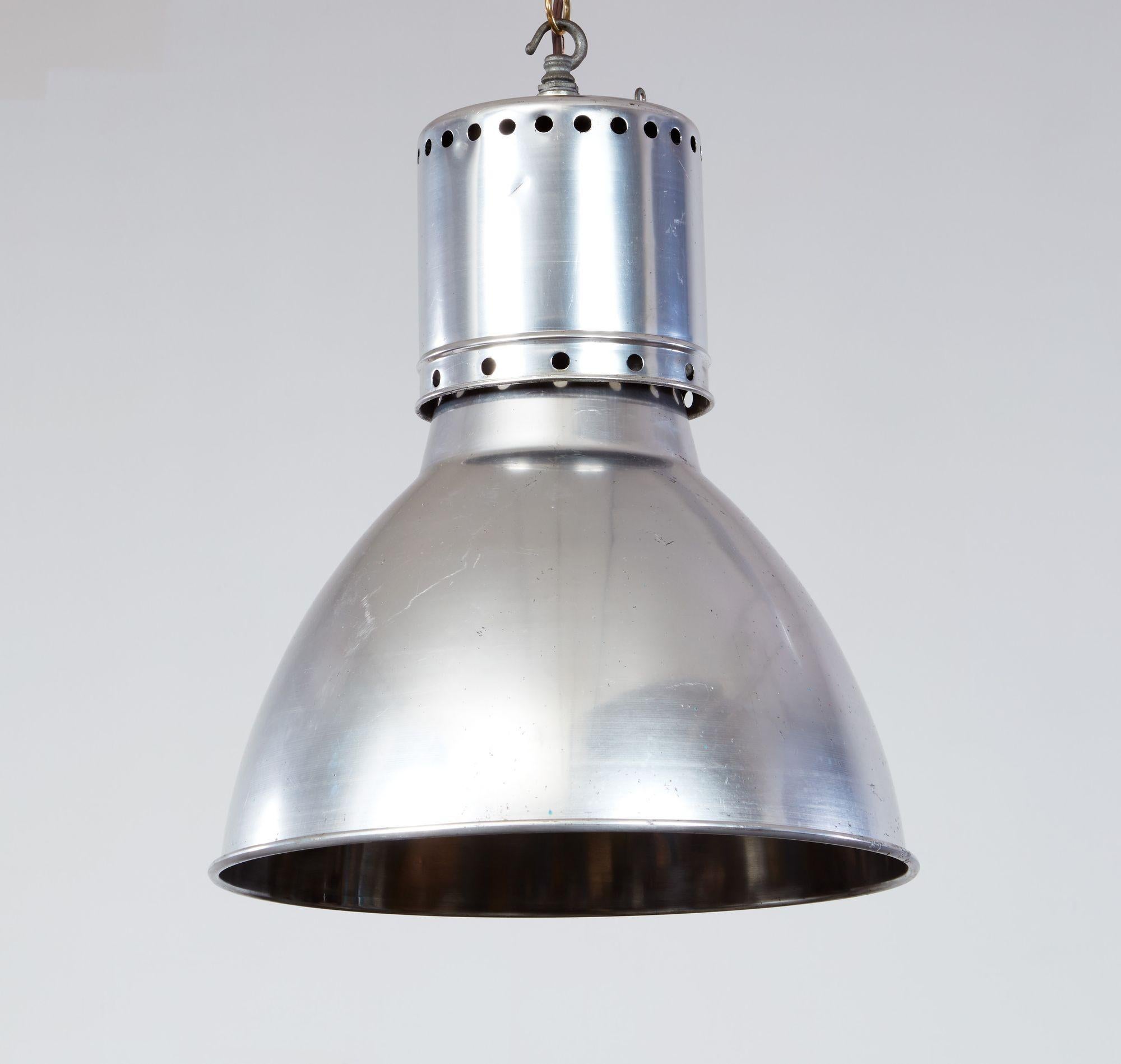 A pair of aluminum pendant lights having cylindrical collars with upper and lower rings of vent holes above concave domes with rolled rims. These are large scale lights from a factory/industrial setting, now suitable for hanging above kitchen