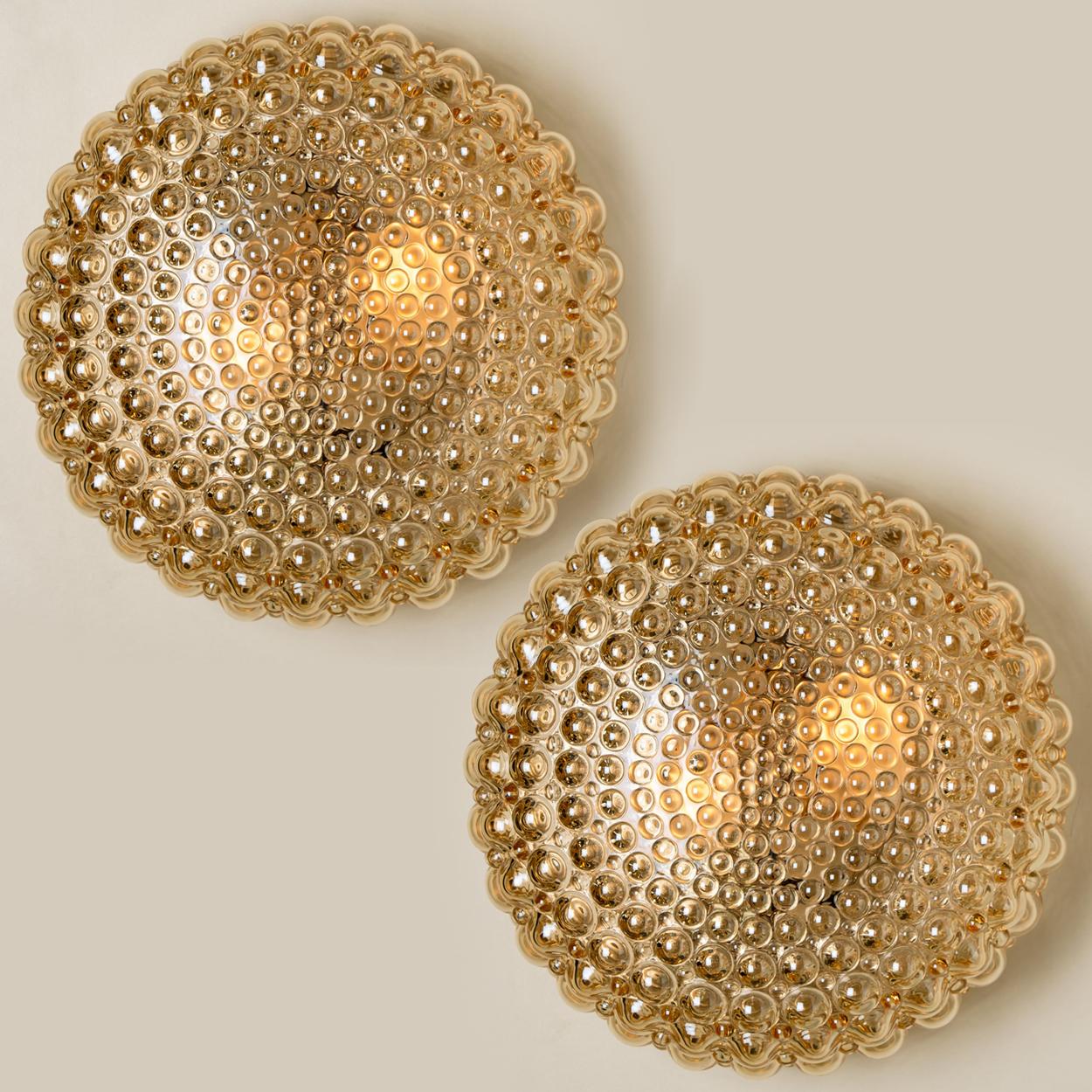 Ein Paar wunderschöne Wandleuchten aus Blasenglas, entworfen von Helena Tynell für Glashütte Limburg. Ein Design-Klassiker, das bernsteinfarbene oder getönte mundgeblasene Glas gibt einen wunderbaren und warmen Schimmer. 

Schwere Qualität und