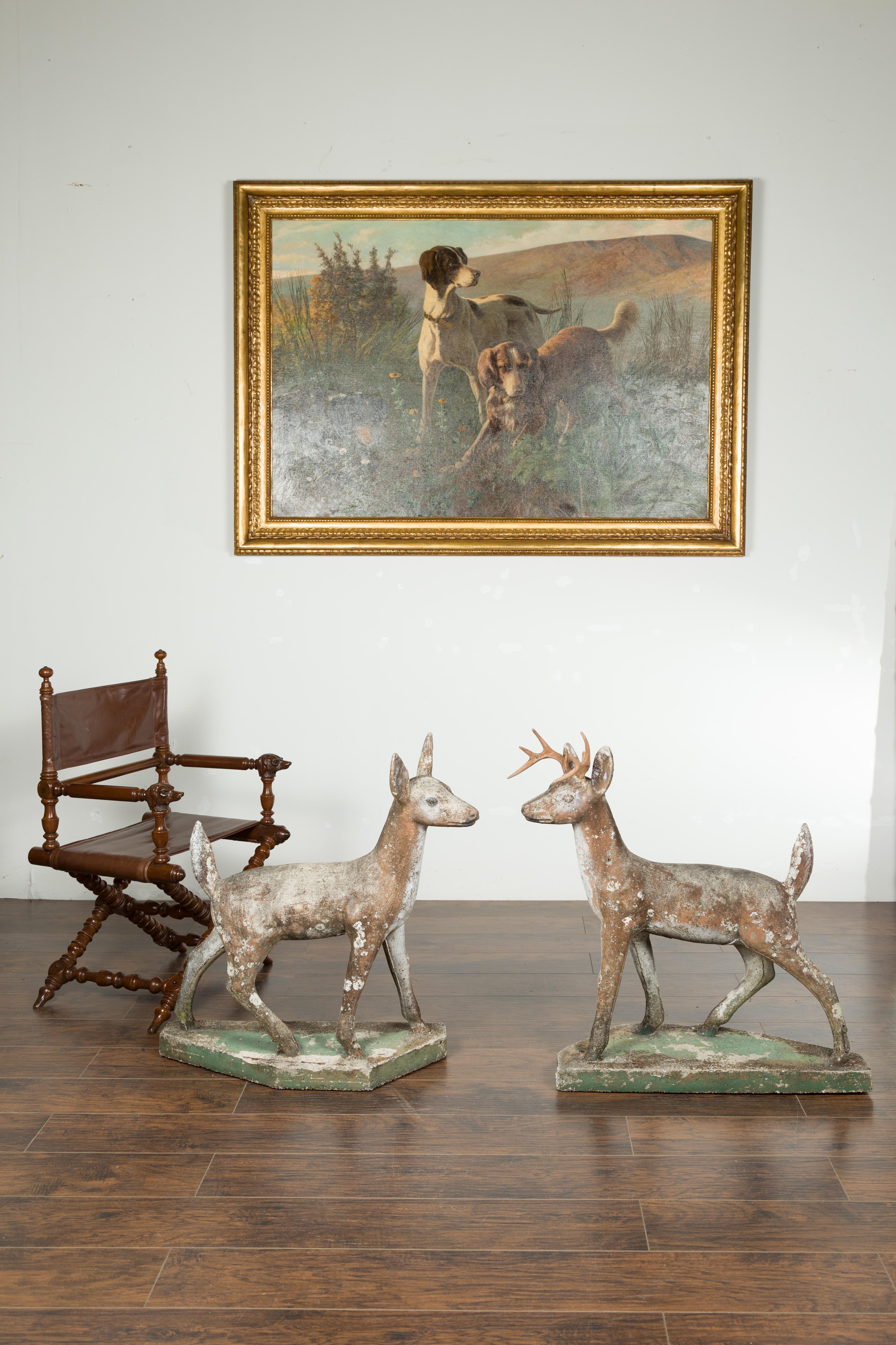 A pair of American concrete deer from the mid 20th century, with antlers and green base. Made in the USA during the second quarter of the 20th century, this pair of concrete sculptures depicts a stag and a doe resting on a green polygonal base.