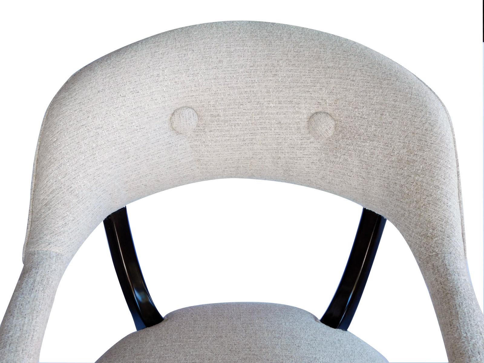 Each with incurved padded back joining padded arms; raised on curved upright supports above a tight seat; all raised on splayed legs.