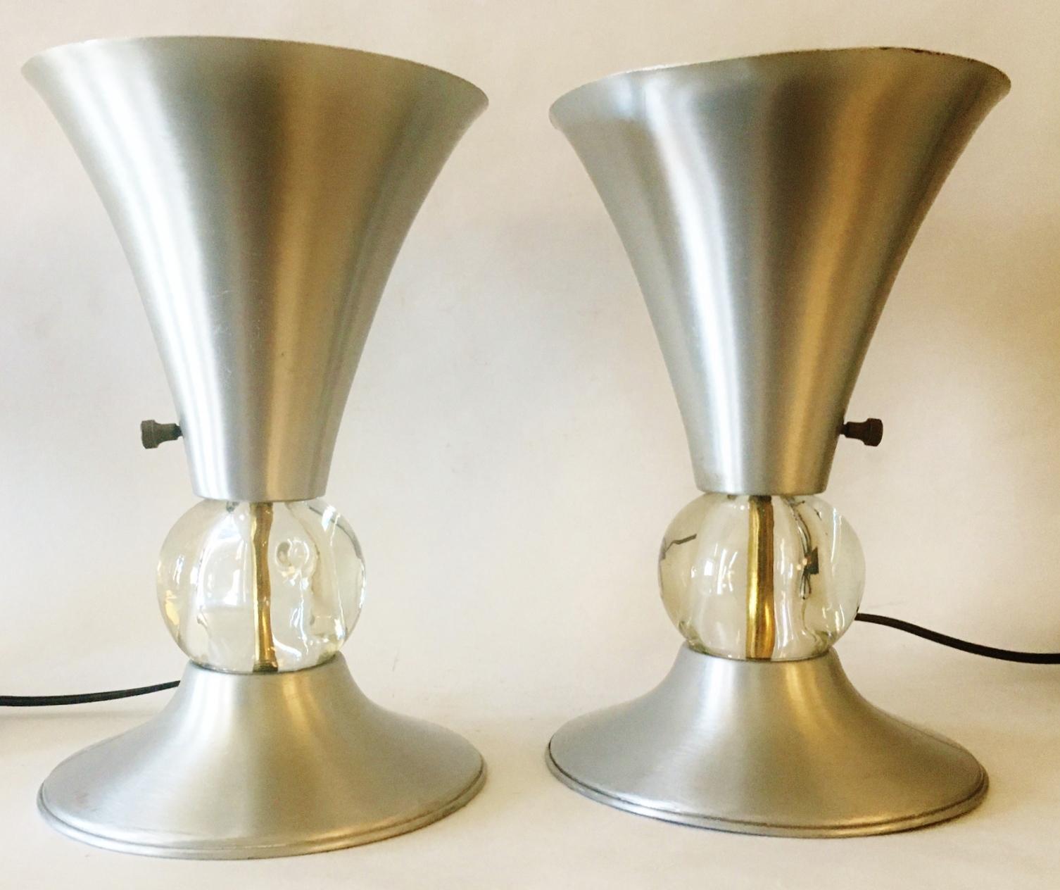 This hard to find pair of American Art Deco spun aluminum small table torchiers have unusually flared and ridged bases that support their equally flared trumpet torchiere shades. The spun aluminum shades and bases are each intersected by 3