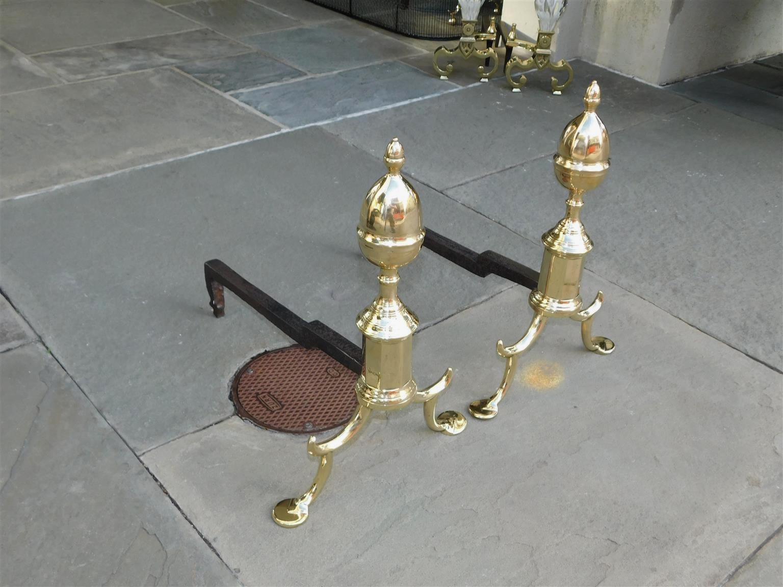 Pair of American brass flanking acorn faceted finial andirons with turned faceted plinths, scrolled spur legs, and resting on penny feet, New York. Late 18th century.