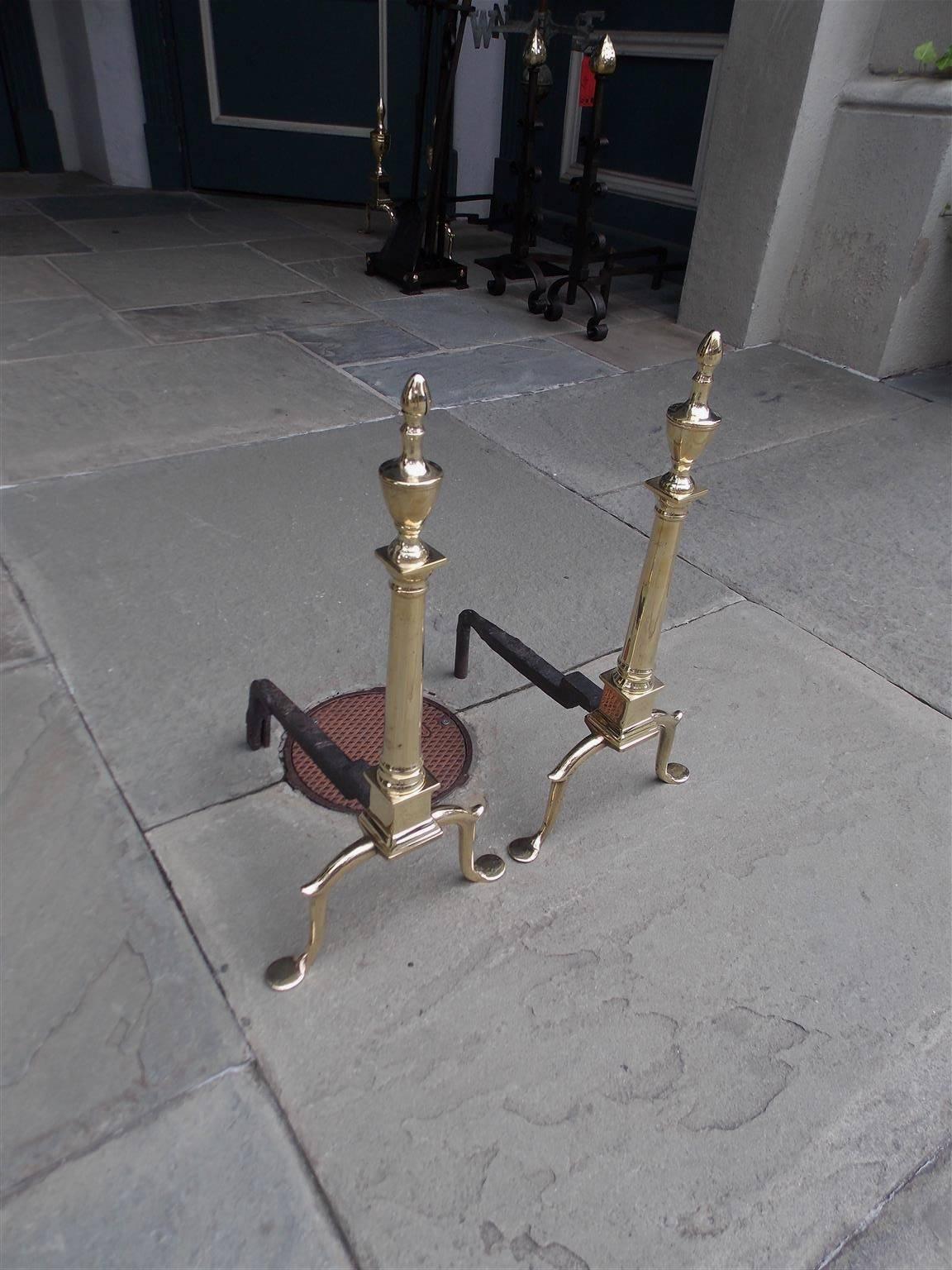 Pair of Graceful American brass and wrought iron andirons with urn finials, circular columns, squared plinths, straight skirts, spur legs, and terminating on step back penny feet, Late 18th century, Philadelphia.