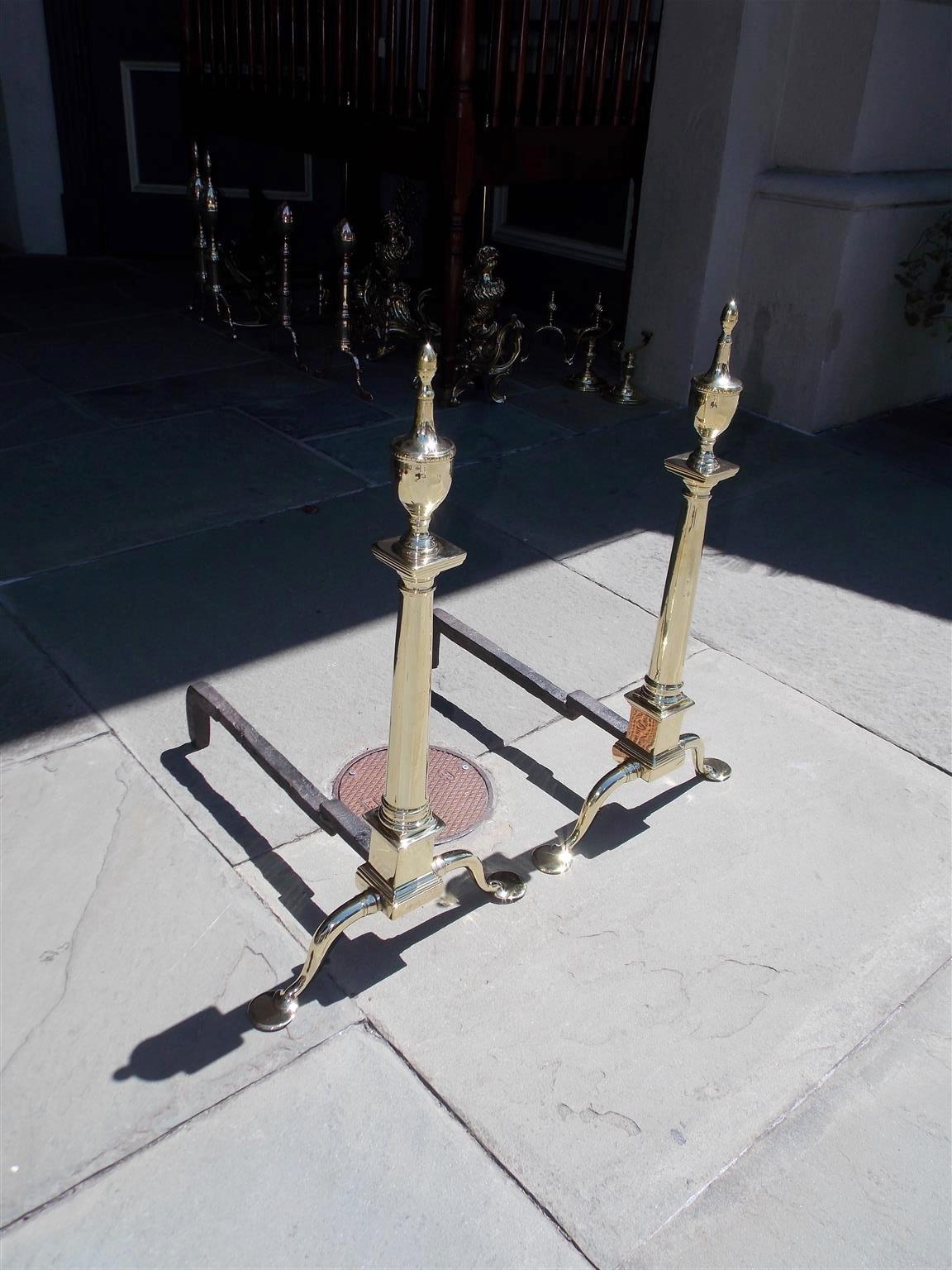 Pair of Graceful American brass and wrought iron andirons with flanking engraved urn finials, centered circular columns, squared block plinths, straight skirts, and terminating on the original step back penny feet, Late 18th century. Philadelphia,