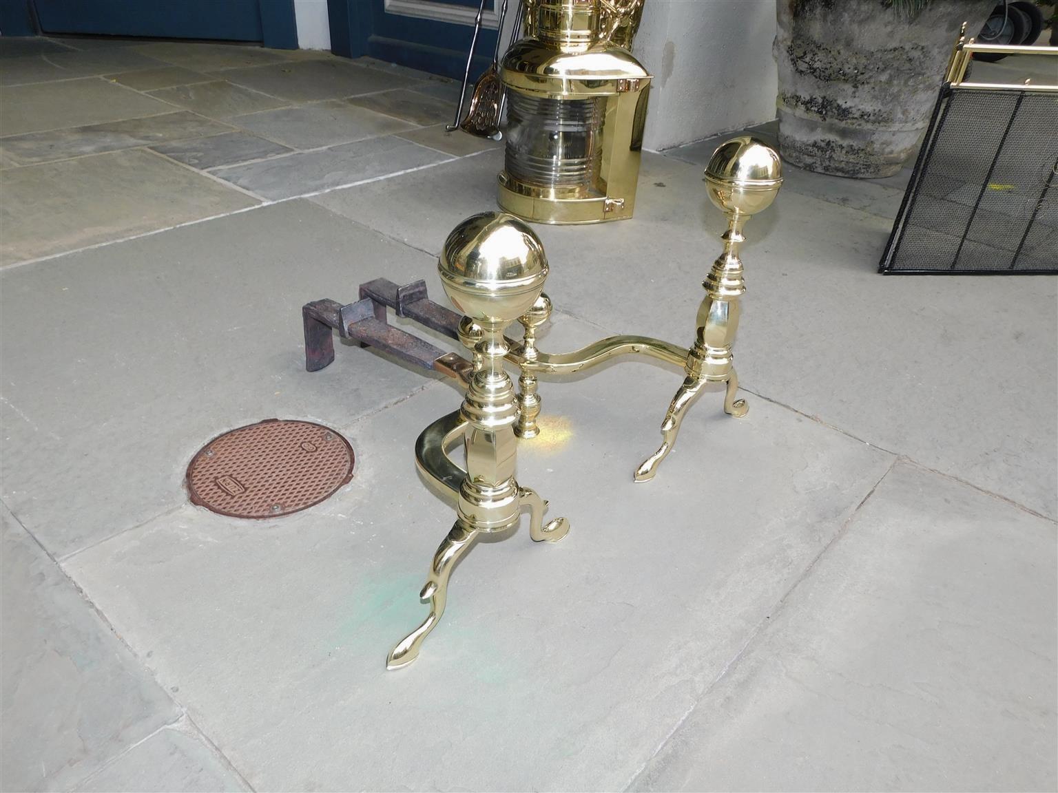 Pair of American brass ball banded finial andirons with ringed turned faceted plinths, supporting curvature matching ball log stops, original rear wrought iron dog legs, and resting on double spur legs with slipper feet. Stamped John Molineux,