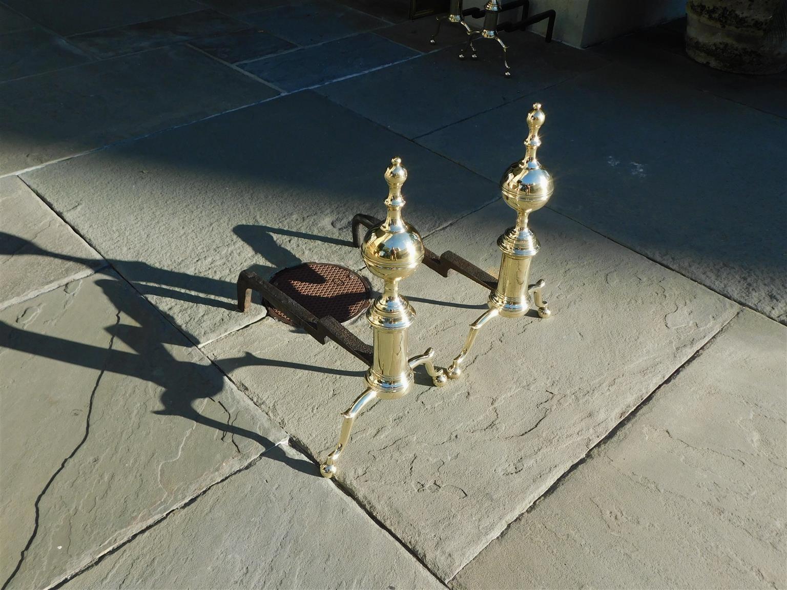 Pair of American brass flanking ball banded finial andirons with circular plinths, spur legs, original wrought iron rear dog legs, and resting on ball feet. Boston, mass. Early 19th century.