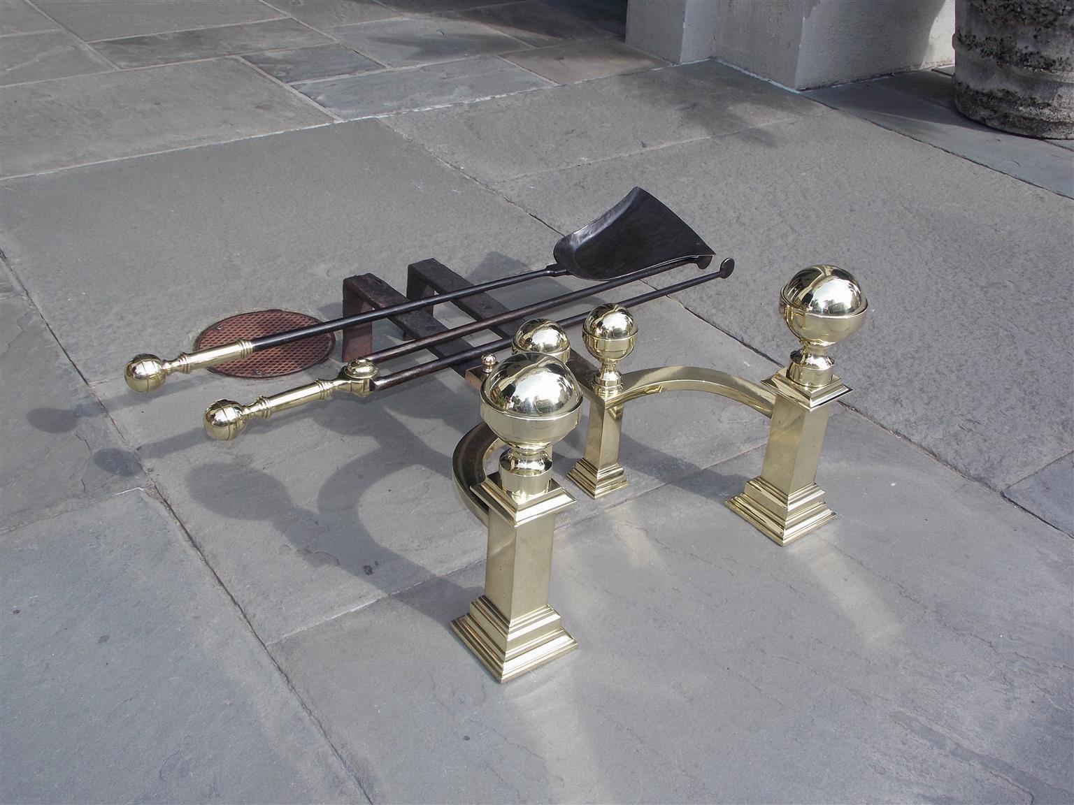Pair of American brass banded ball top andirons with squared centered plinths, step back molded edge bases, curvature matching log stops, and the original wrought iron dog legs. Stamped by maker John Hunneman, Boston. Andirons have original matching