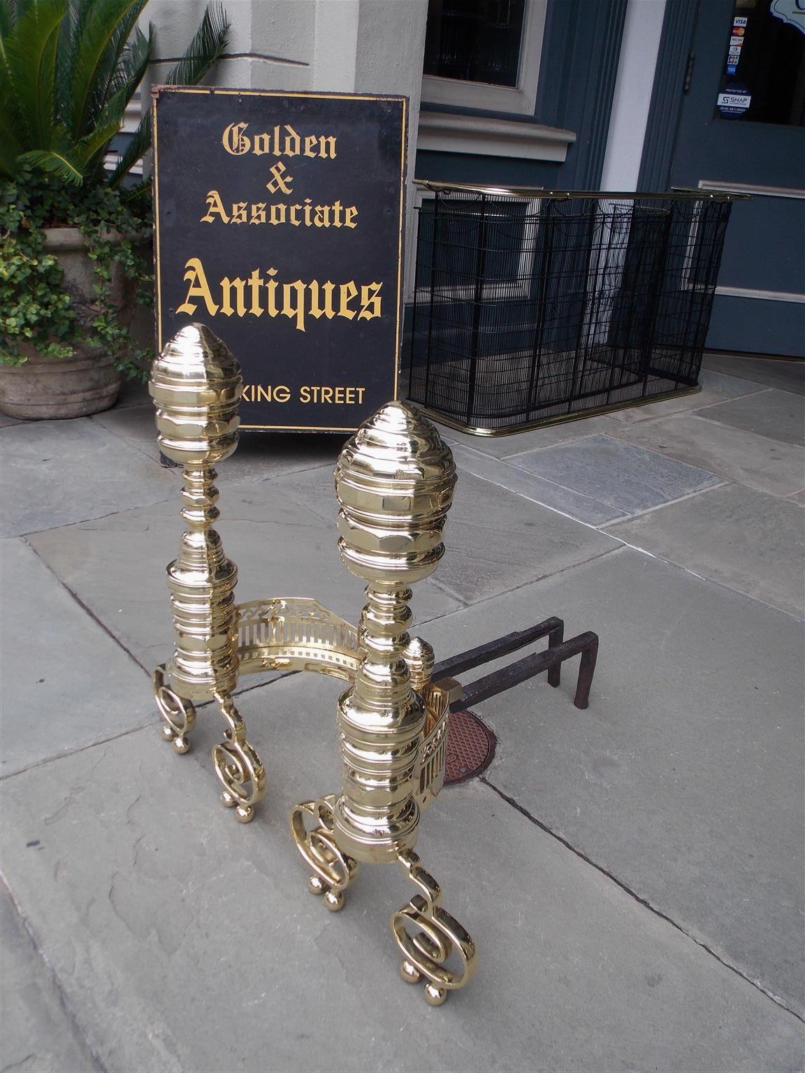 Pair of Important size American brass Empire andirons with faceted ribbed finials, turned ringed centered columns, faceted ribbed plinths, flanking pierced scrolled galleries, matching finial log stops with turned brass legs, and terminating on