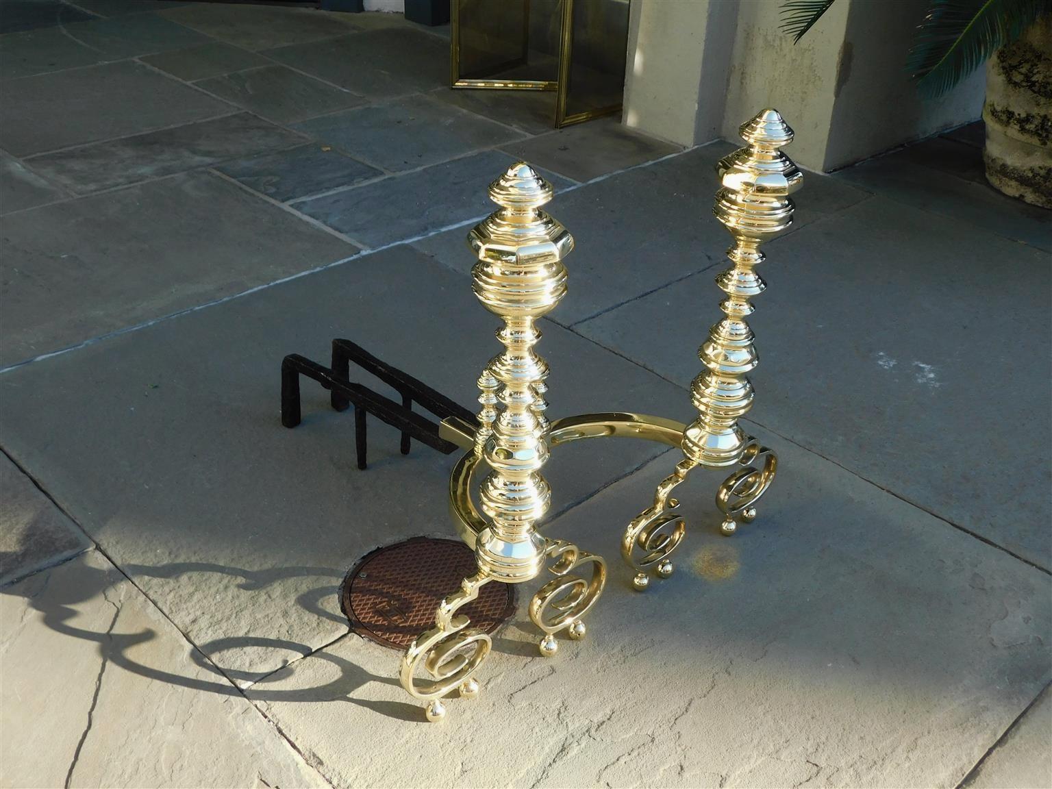 Pair of American brass flanking faceted finial andirons with centered turned faceted columns, meticulously turned matching log stops, original wrought iron rear dog legs, and resting on scrolled legs with double ball feet. Philadelphia, Early 19th