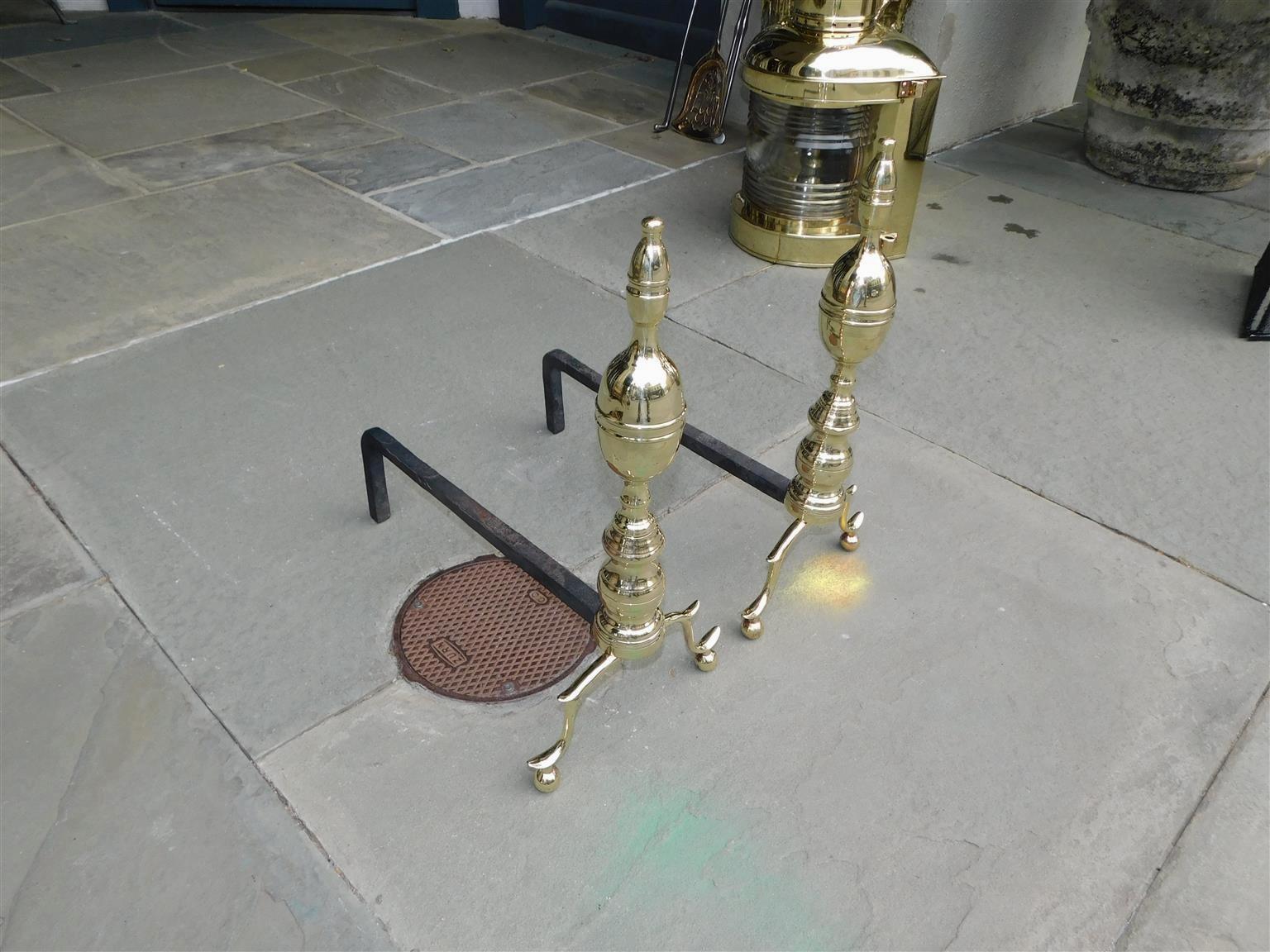 Pair of American brass banded flanking lemon on lemon finial andirons with turned bulbous plinths, original rear wrought iron dog legs, and resting on double spur legs with ball feet. New York, Early 19th Century.