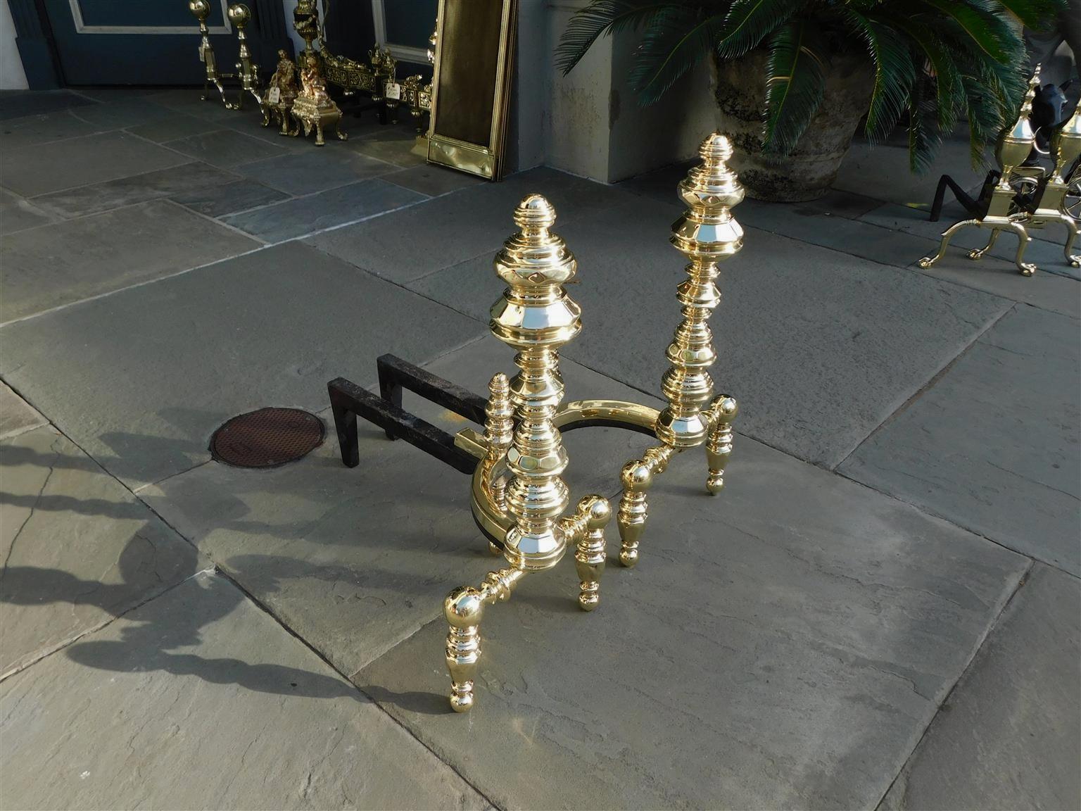 Pair of American brass flanking urn faceted finial andirons with bulbous squared faceted legs, matching faceted bulbous log stops, and resting on the original wrought iron rear dog legs, early 19th century Stamped by maker E. Smylie, New York.