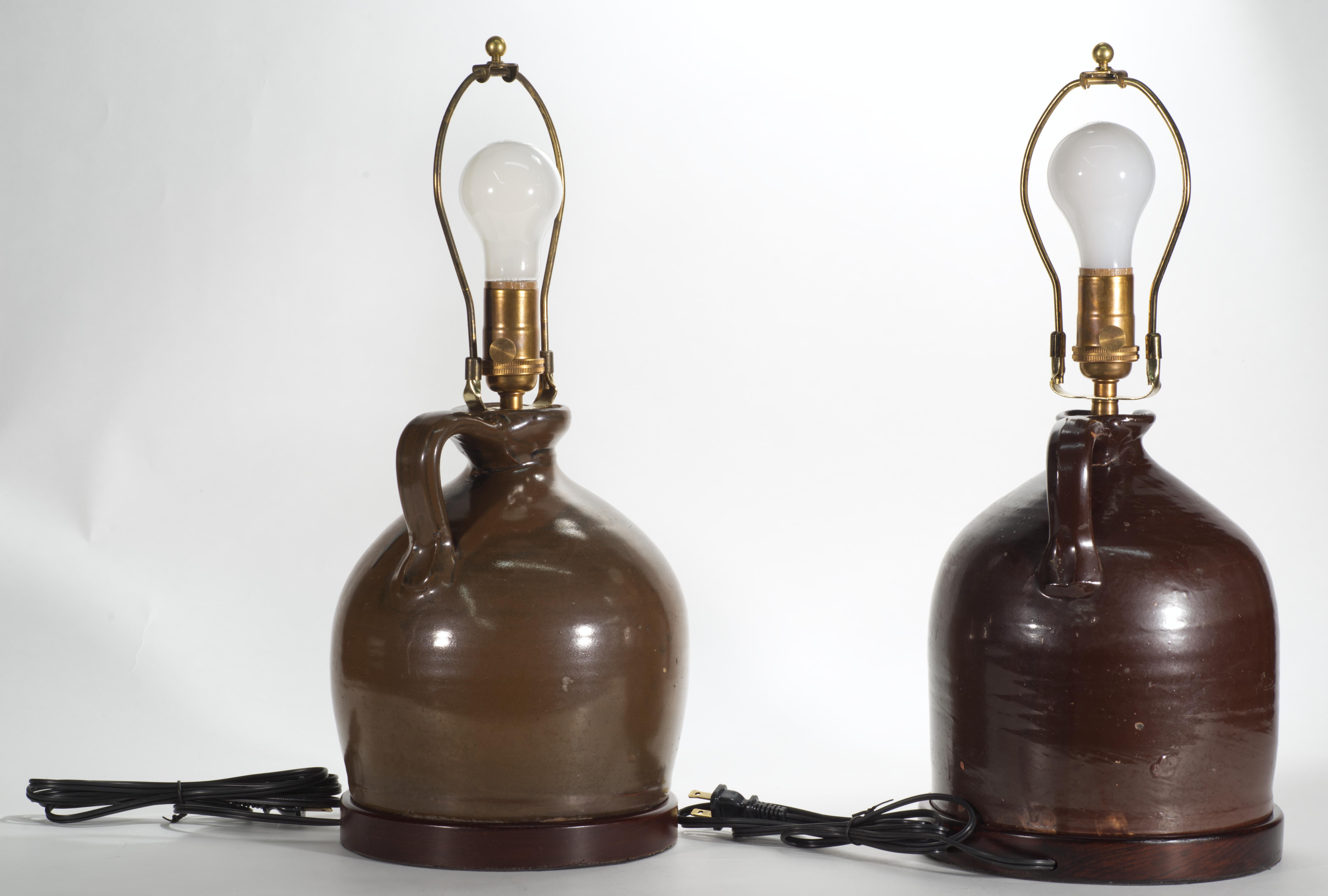 Pair of antique brown glazed stoneware jugs, converted into table lamps, feature traditional shape with applied finger ring handles, rounded shoulders, and narrow necks; they are decorated in rich, earthy brown glaze. The lamps have been mounted on