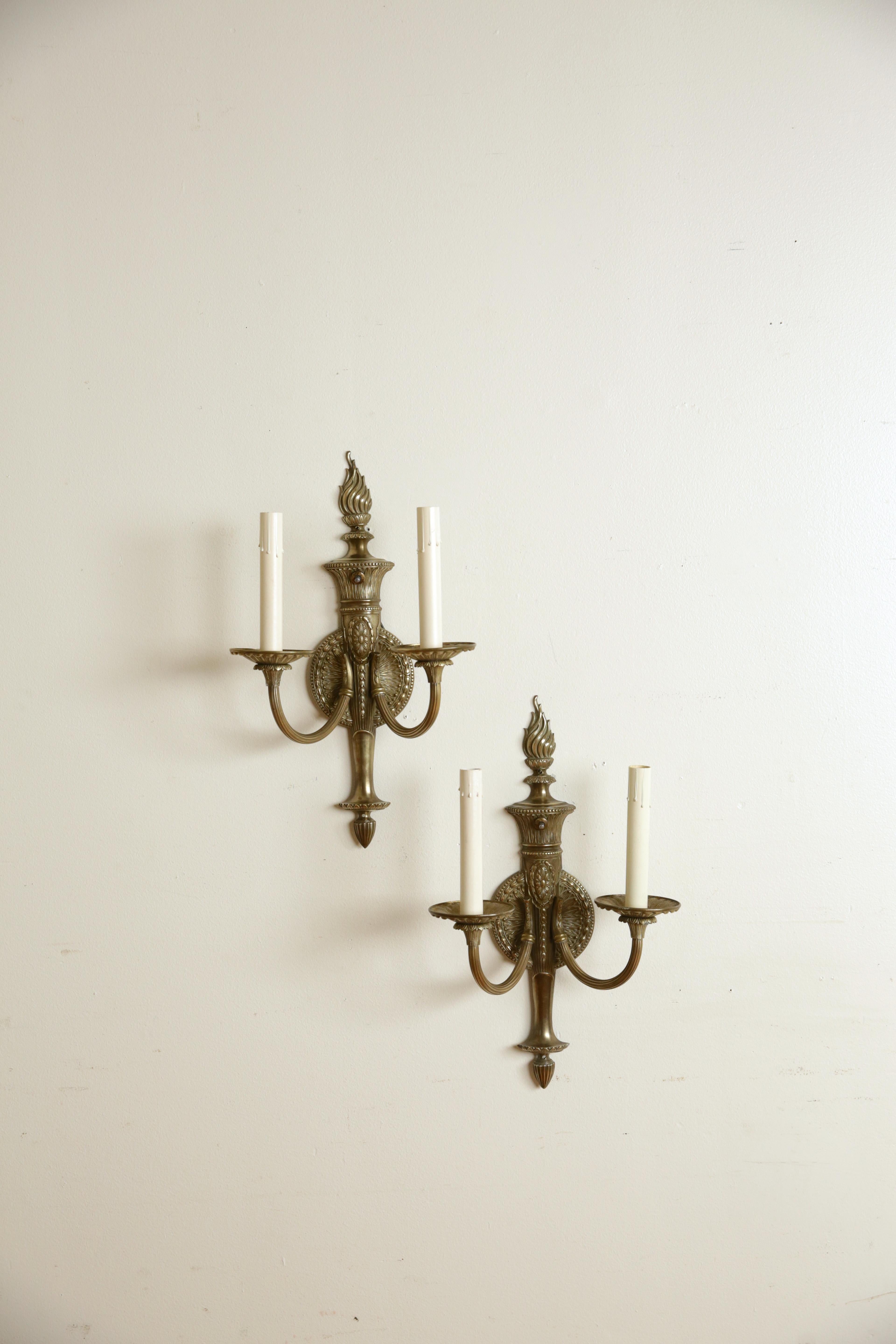 Chaque applique est joliment moulée et présente des corps de style torchère avec des fleurons en forme de flamme sur des plaques arrière circulaires, les plaques arrière émettant des bras courbés avec de grandes pampilles, conservant les
