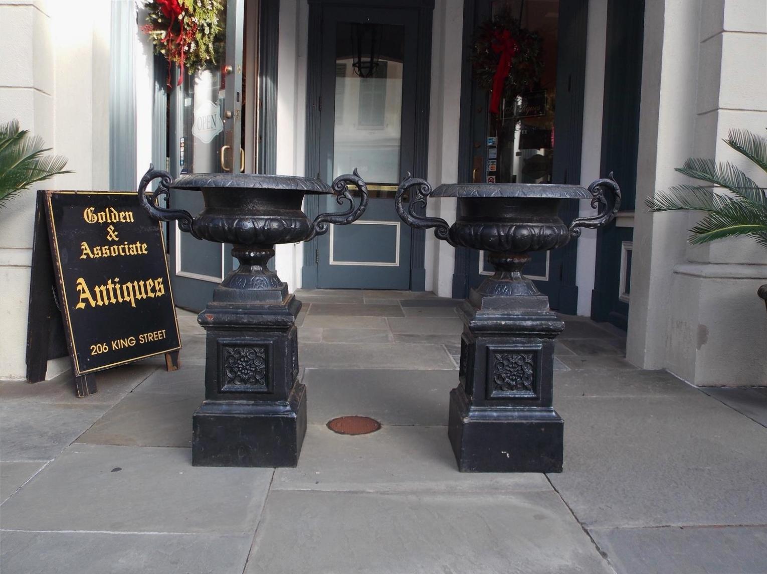 Pair of American cast iron and painted campana-form floral garden urns with an incised molded edge, flanking acanthus side handles, and resting on decorative squared floral plinths. Late 19th Century.  Urns separate from plinths for shipping and