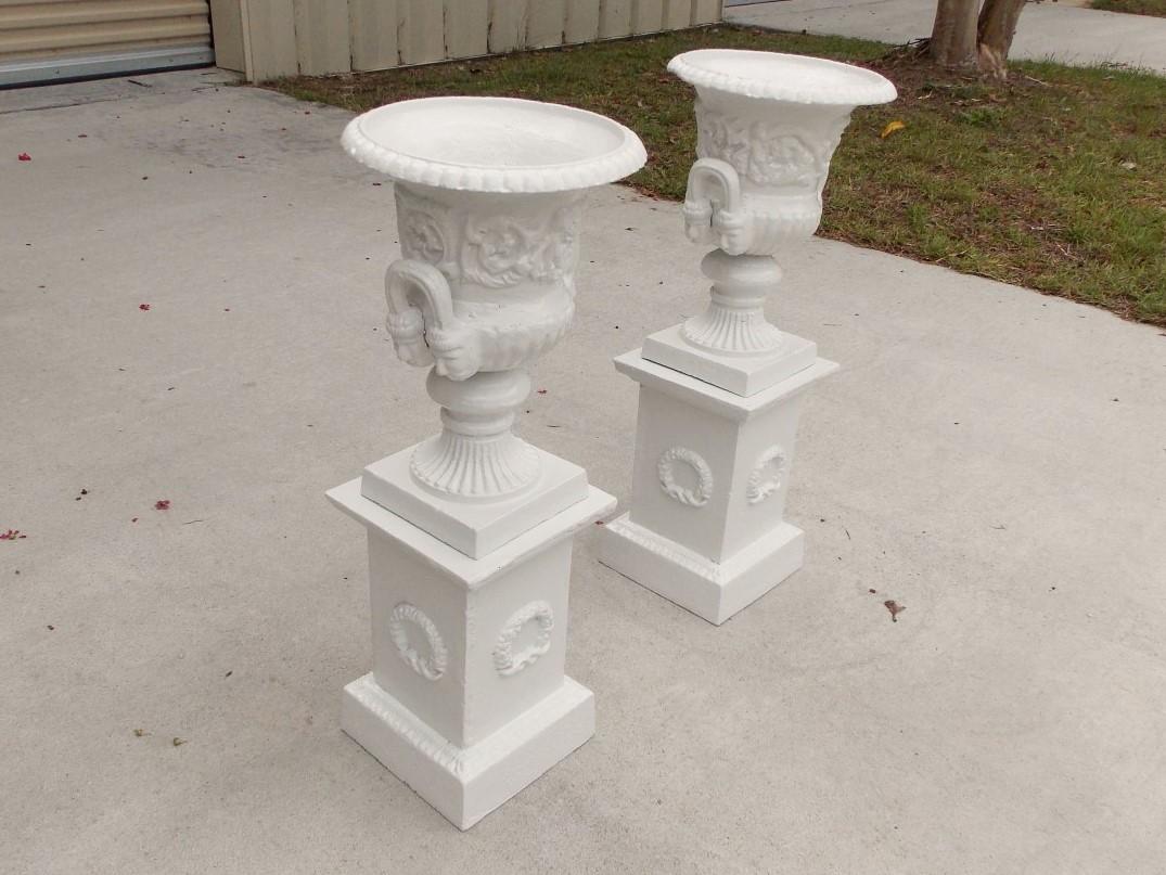 Pair of American cast iron powder-coated floral Campana garden urns with an egg and dart molded edge, flanking figurative side handles, fluted squared bases, and resting on squared plinths with decorative flanking laurel wreaths, Late 19th century.