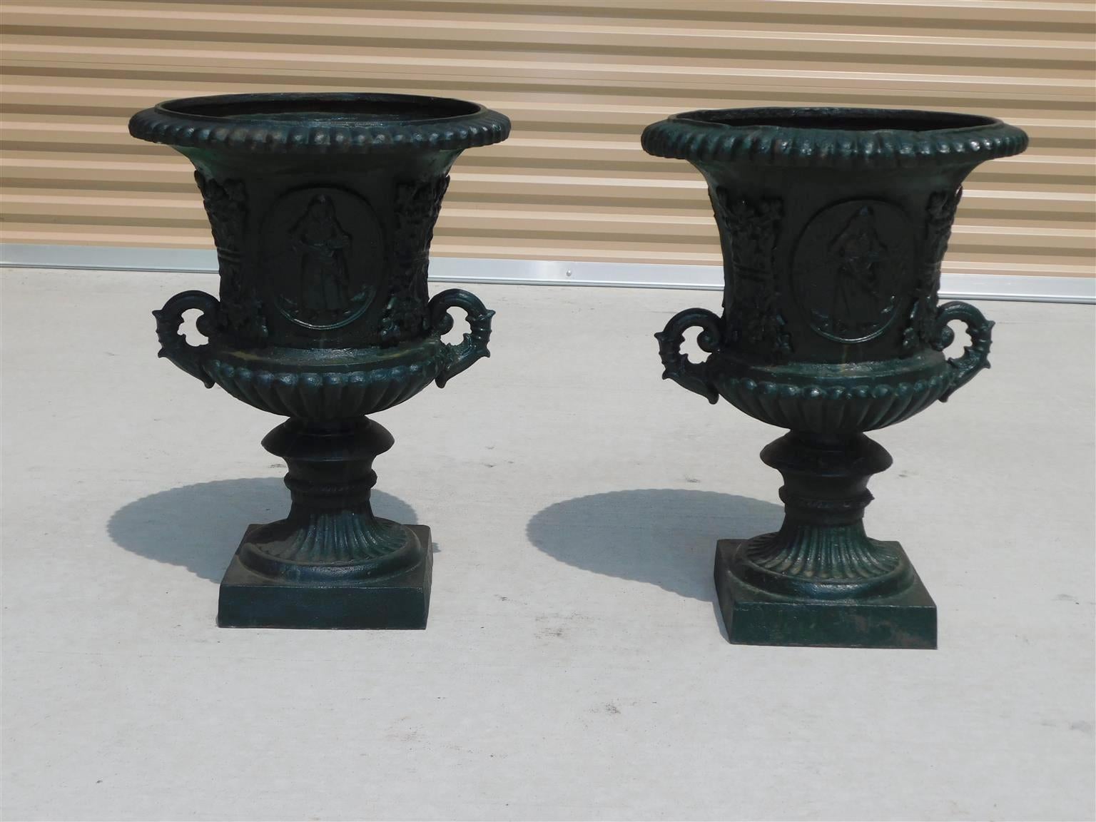 Pair of American Classical figural and foliage painted campana form garden urns with flanking foliage side handles and resting on circular fluted squared plinths, Mid 19th Century
Pair Urn measurements: 26.25