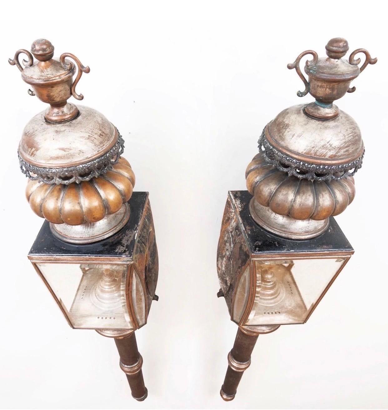 Pair of American coach lanterns with urn finials, floral swag motif, and original beveled glass. Unpolished patina. Rewired and ready to go.