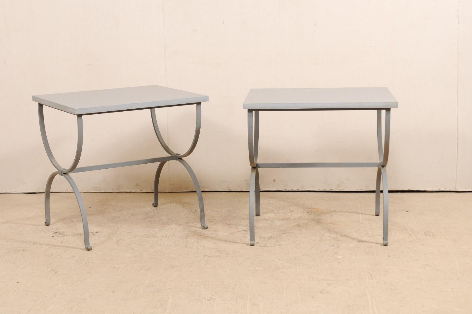 A pair of American custom iron occasional tables with stone tops. This pair of custom side tables each feature a rectangular-shaped, honed quartzite top, supported by a painted iron savanrola, or curule style base. The honed stone top is a light