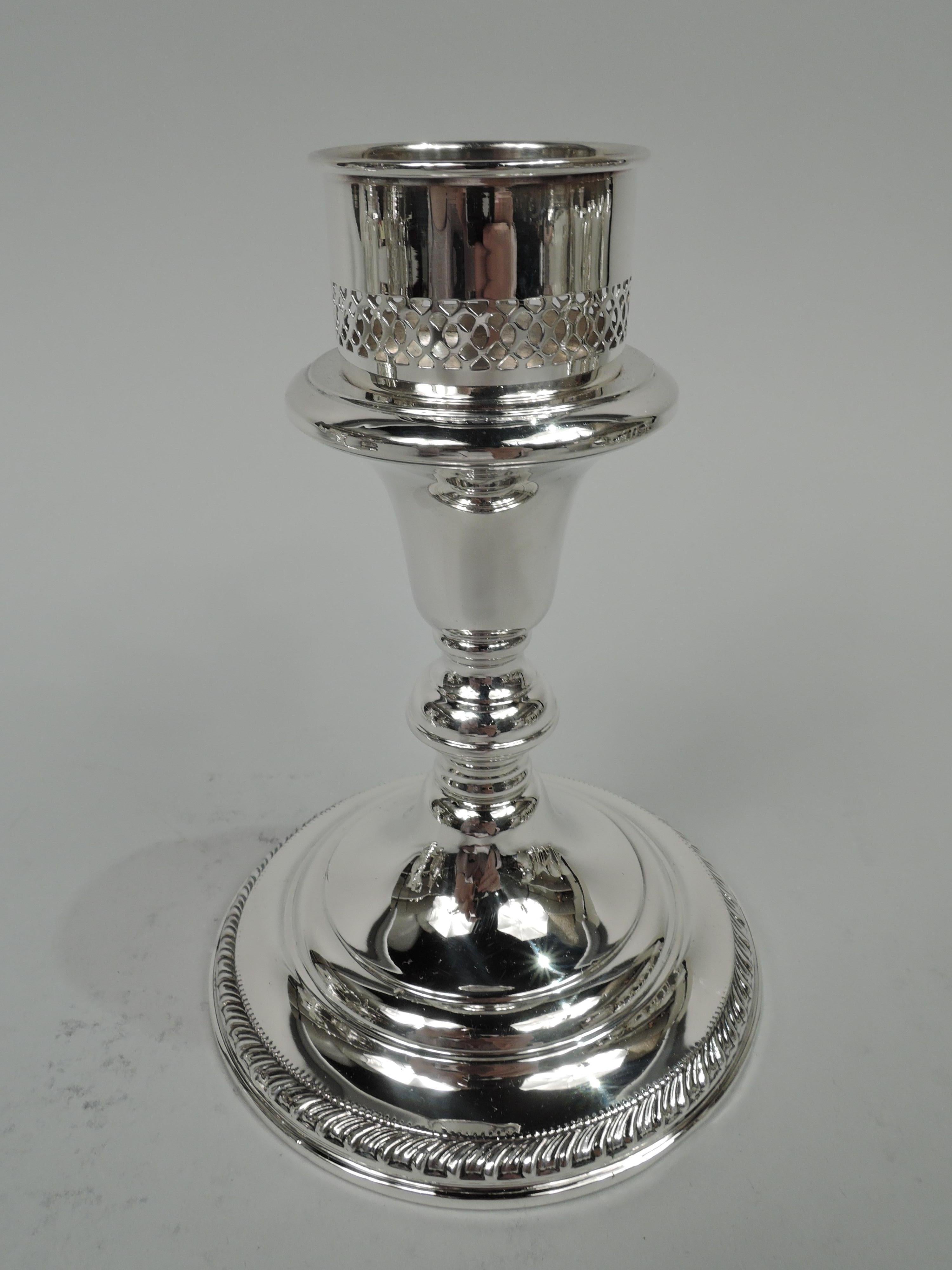 Pair of Edwardian Classical sterling silver candlesticks. Made by Redlich in New York. Each: Tapering socket mounted with pierced, inset, and straight sides; knop on domed foot. Beading and gadrooning. Fully marked including maker’s and retailer’s