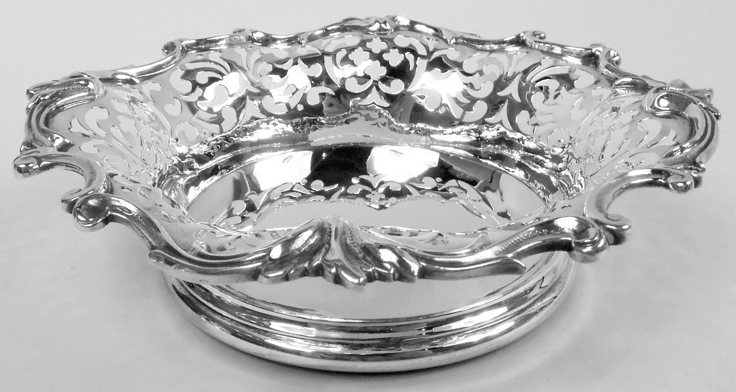 Par de posavasos clásicos eduardianos de plata de ley para botellas de vino. Fabricado por Dominick & Haff en Nueva York, hacia 1910. Cada una: Pozo macizo; los lados tienen volutas de hojas caladas y el borde acampanado con volutas y hojas