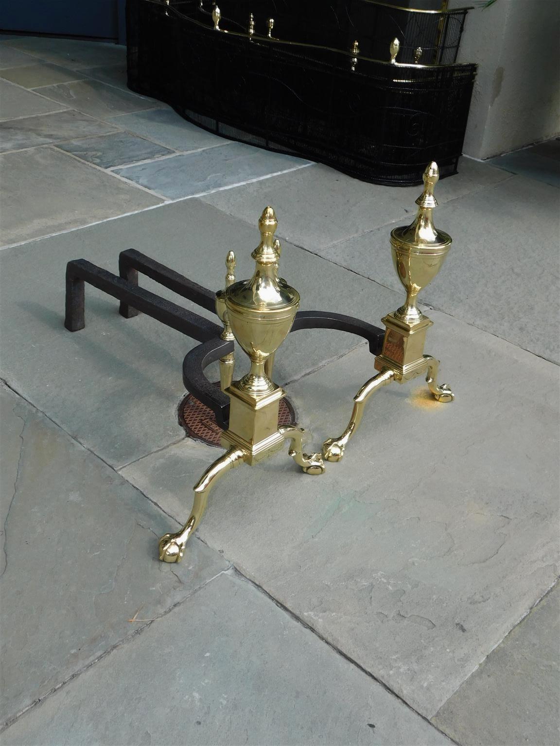 Pair of American Federal brass andirons with flanking urn finials, matching urn finial log stops, engraved swags on skirt, and resting on banded double spur legs with ball and claw feet. Philadelphia, Early 19th century.