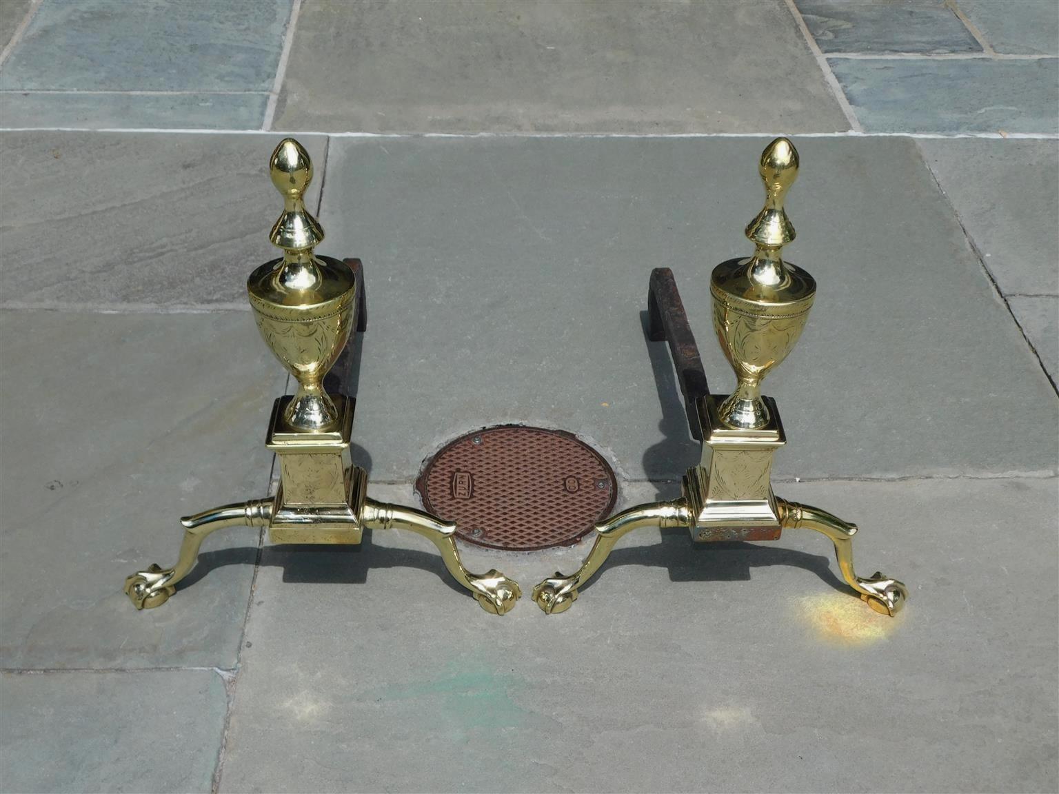Pair of American Federal brass andirons with shield engraved urn finials, shield engraved plinths, incised checkering lines, engraved swags on skirt, and resting on banded spur legs with ball and claw feet. Philadelphia, Early 19th century.