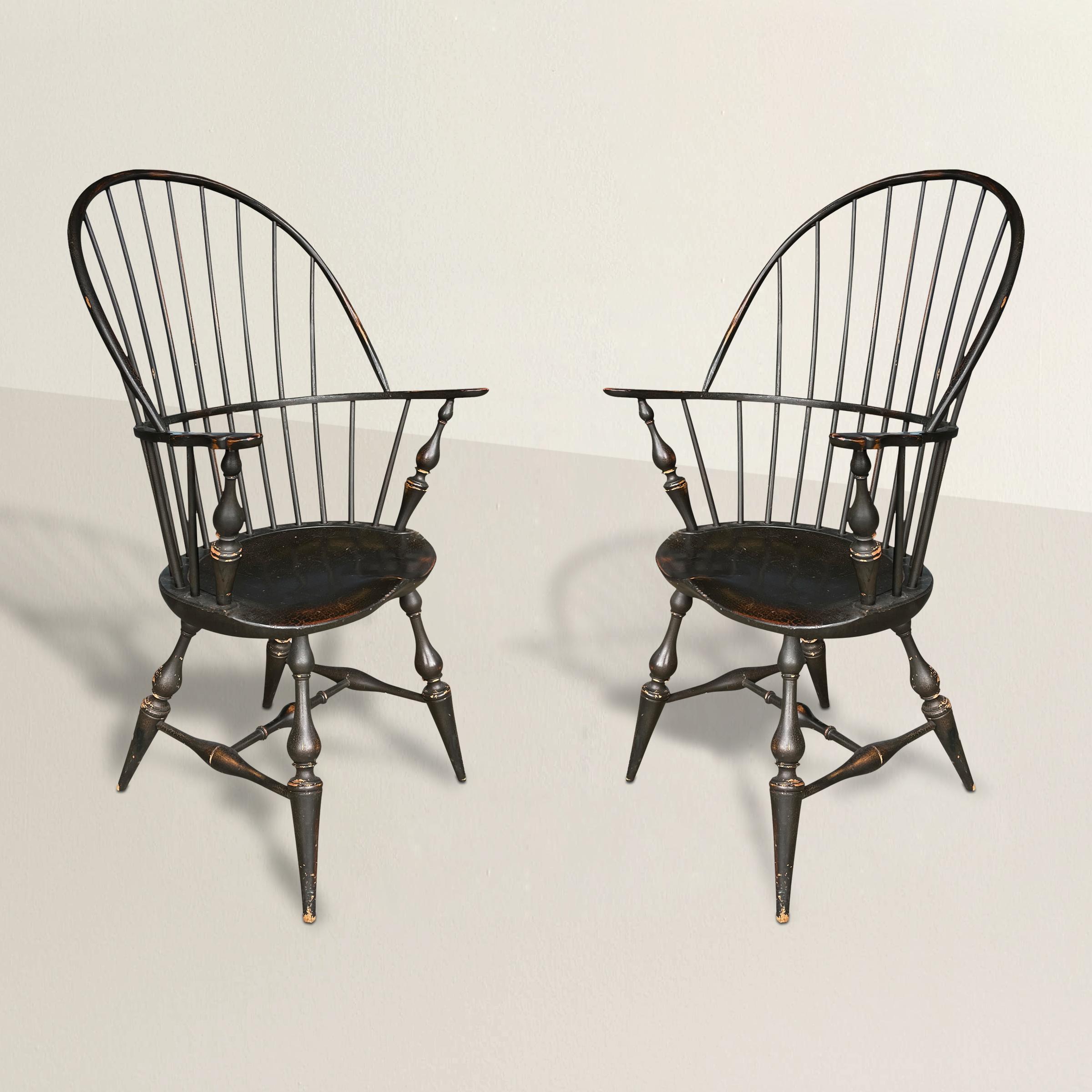 A pair of 20th century American Windsor chairs with continuous hoop backs, saddles seats, turned legs tapering to narrow feet, and their original black painted finishes. Perfect at a dining table, or flanking the fireplace indoor living room.