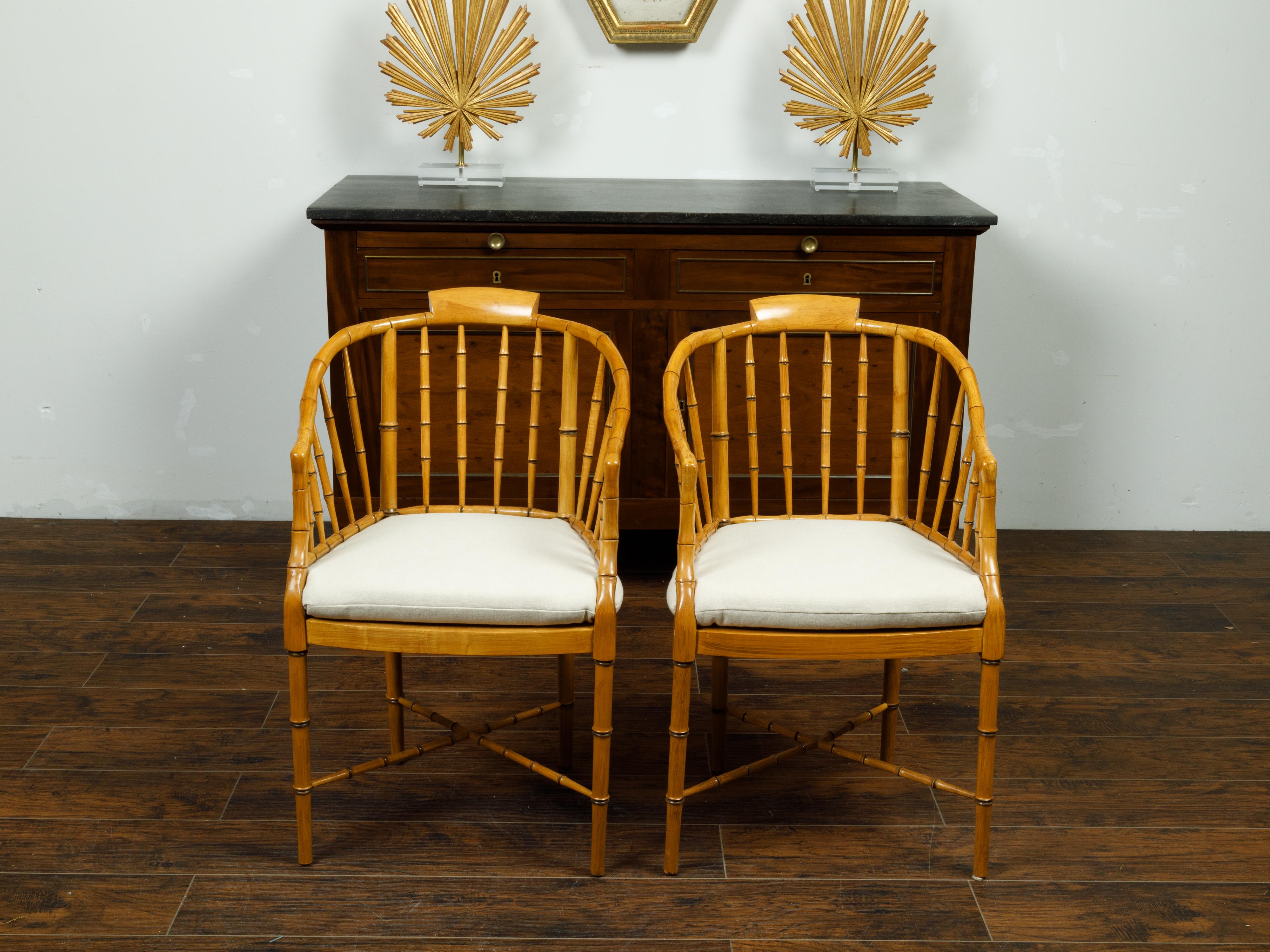A pair of vintage Baker Furniture style faux-bamboo tub armchairs with custom cushions and cross stretchers. Made of faux-bamboo, each of this pair of American Baker style chairs features a tub shaped back and curved arms resting on a cane seat