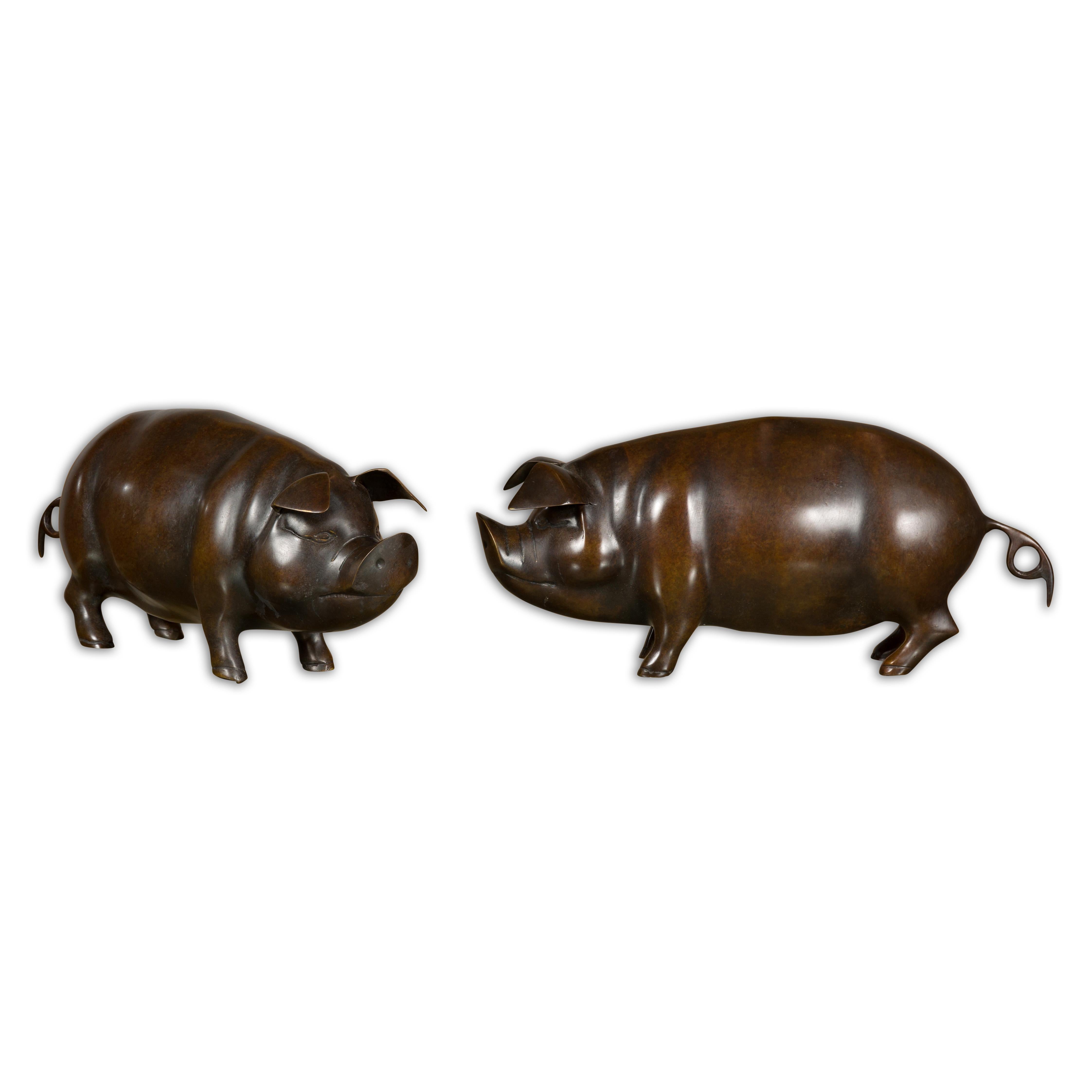 Paire de sculptures de cochons en bronze américain, datant de 1950-1970, à la patine foncée. Ces charmantes sculptures de cochons en bronze américain, datant du milieu du XXe siècle, dégagent du caractère et de la fantaisie dans leurs petites formes