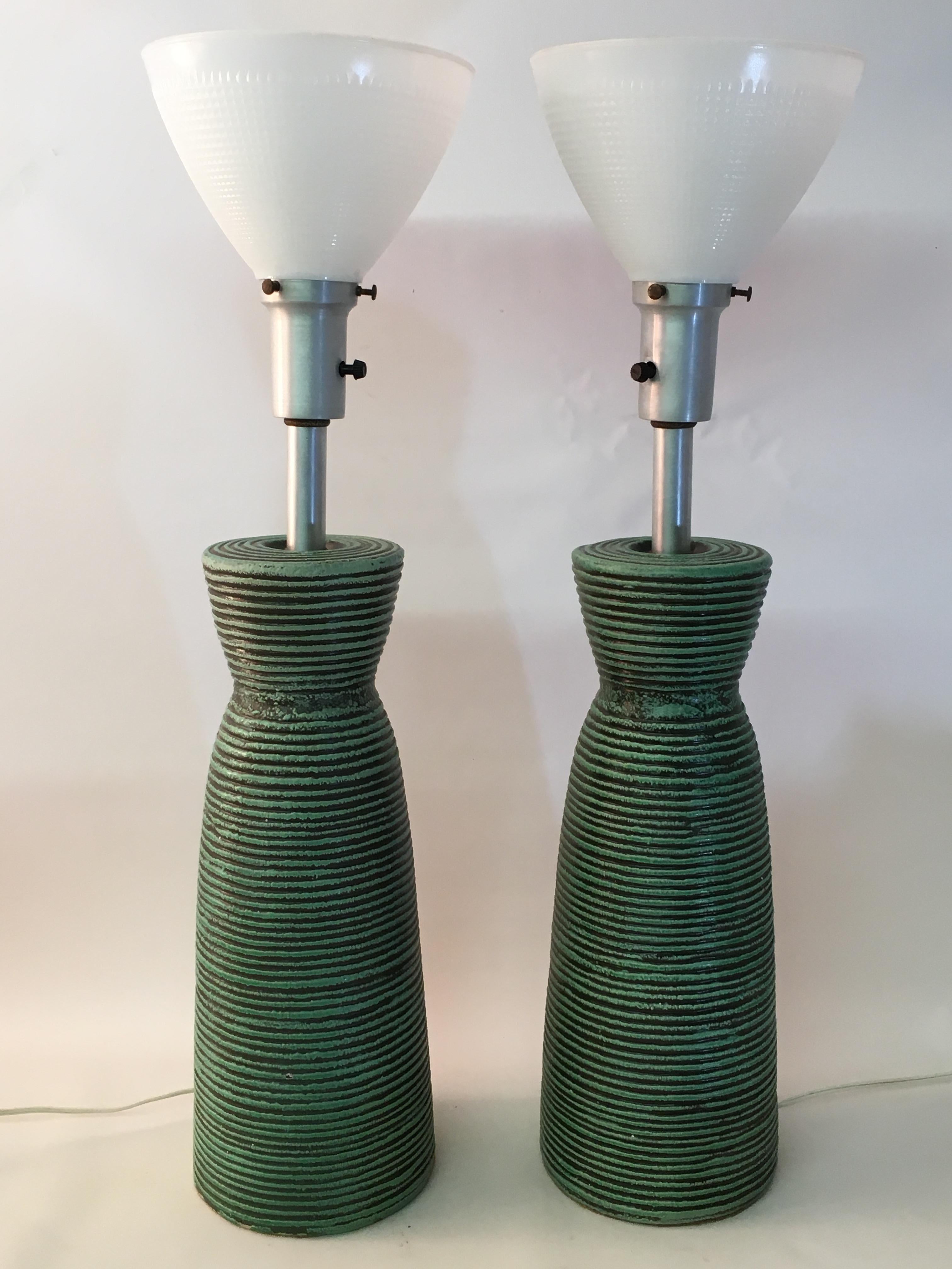 Cast ceramic ribbed and signed Kelby table lamps. Aluminum bulb sockets with white glass diffusers. Tactile raised decoration that ranges from a lighter turquoise/mint green to black glaze, circa 1950. Good working condition. 

Ceramic body