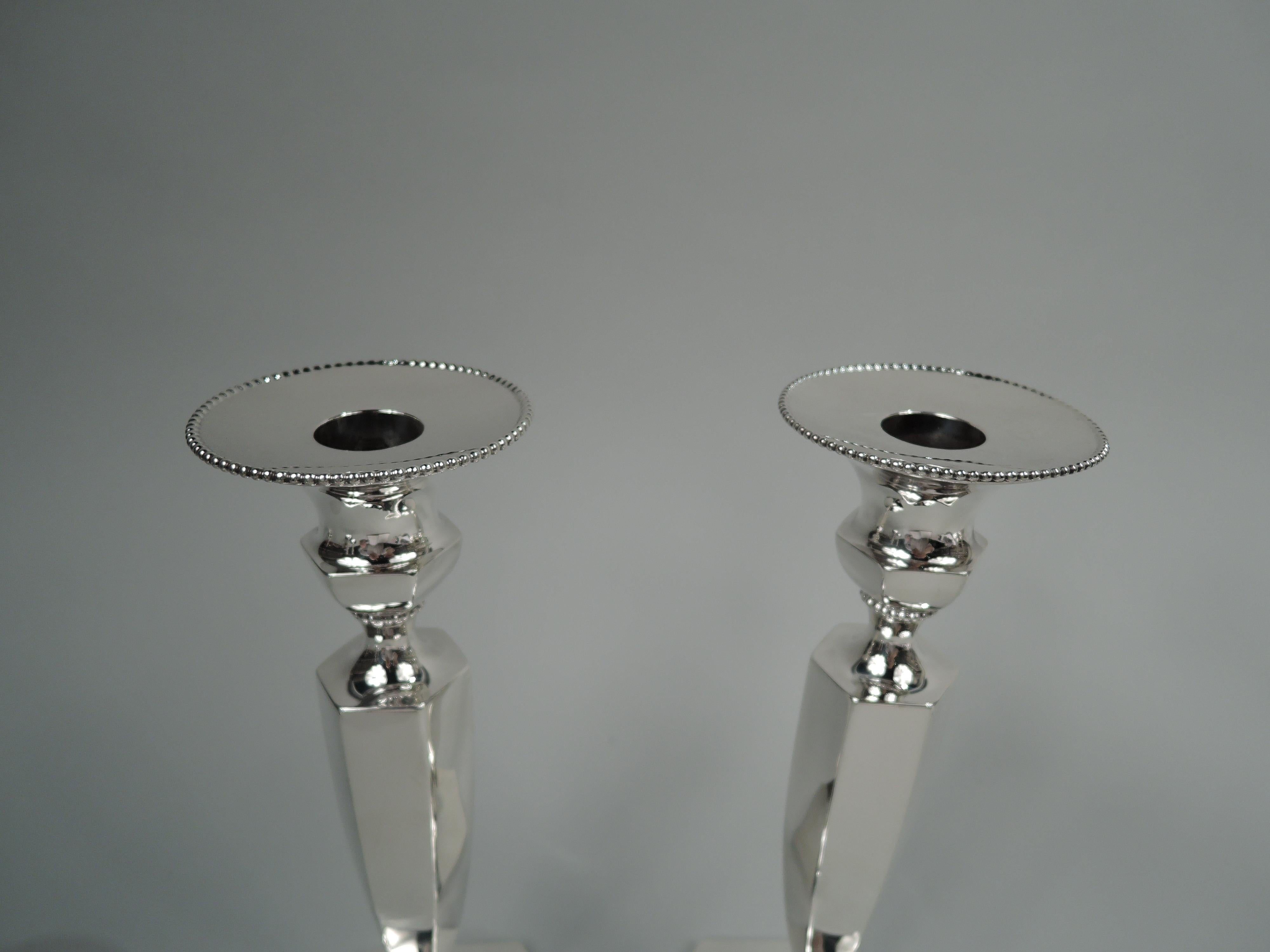 Pair of Modern Georgian sterling silver candlesticks. Made by Roger Williams Silver Co. (later part of Gorham) in Providence, ca 1900. Each: Bellied socket with round detachable bobeche; tapering shaft on raised foot. Beaded and faceted. Fully