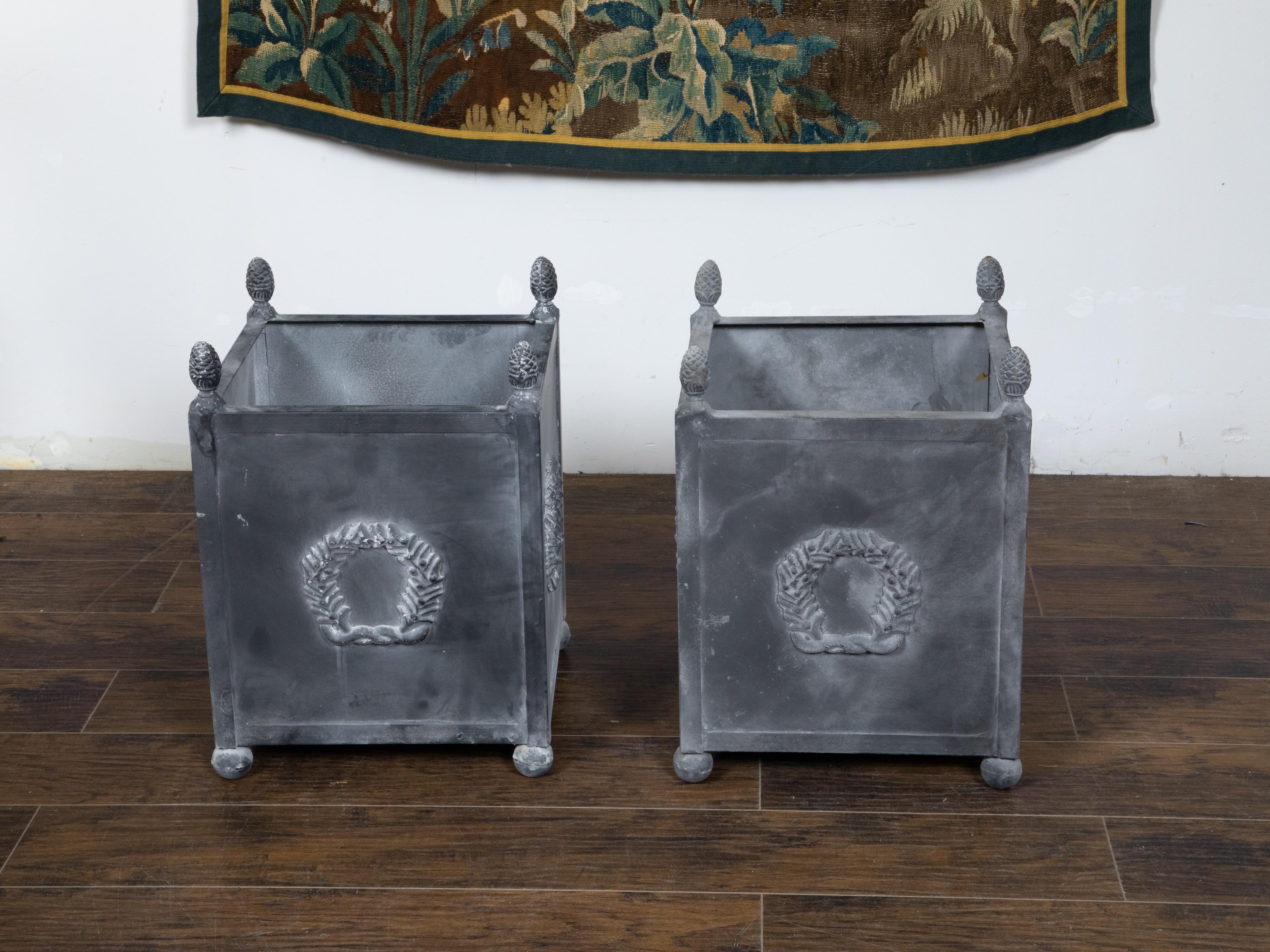 A pair of vintage American Neoclassical inspired metal cache pot planters from the 20th century with grey patinated color, laurel wreath motifs, acorns and petite ball feet. Made in the USA during the 20th century, each of this pair of metal