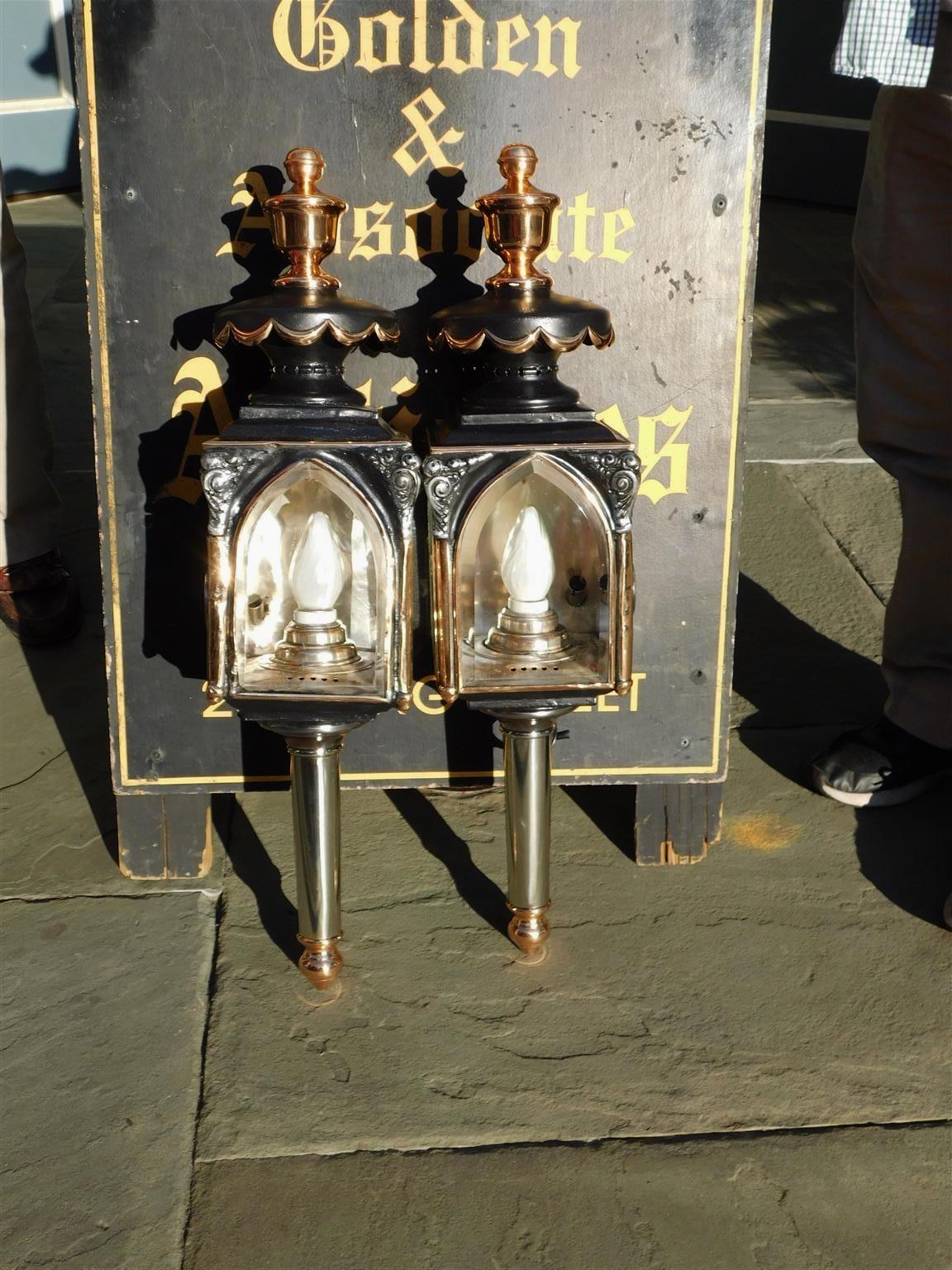 Pair of American nickel silver over copper & brass coach lanterns with urn finials, floral swag motif, and resting on a turned bulbous tapered ringed reservoir. Coach lanterns have the original beveled glass and are signed by the maker James