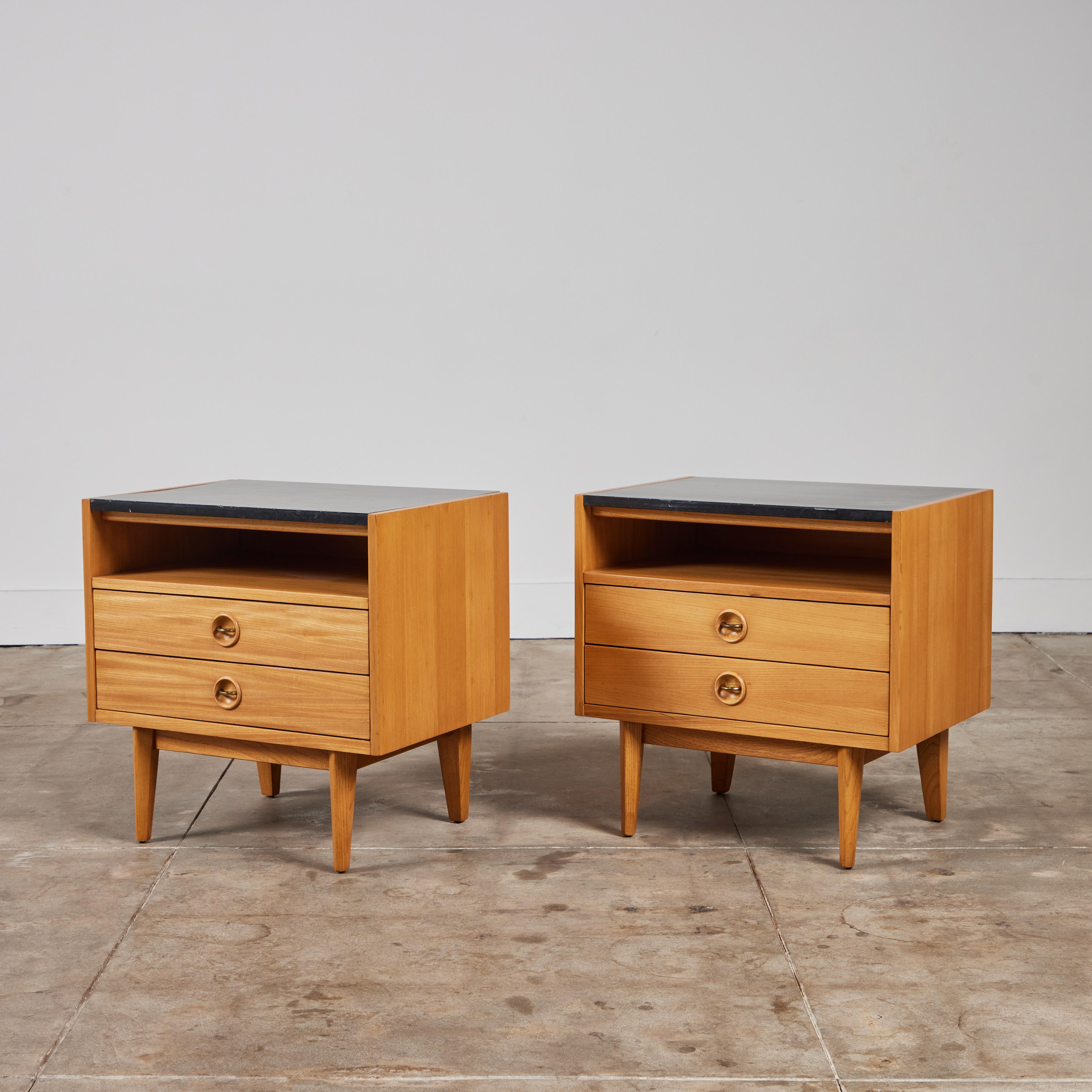 Pair of oak American of Martinsville night stands, c.1950s, USA. This minimal design features black laminate surface, two drawers with curved brass drawer pulls and an open shelf between the table top and drawers. The nightstands rest upon slightly