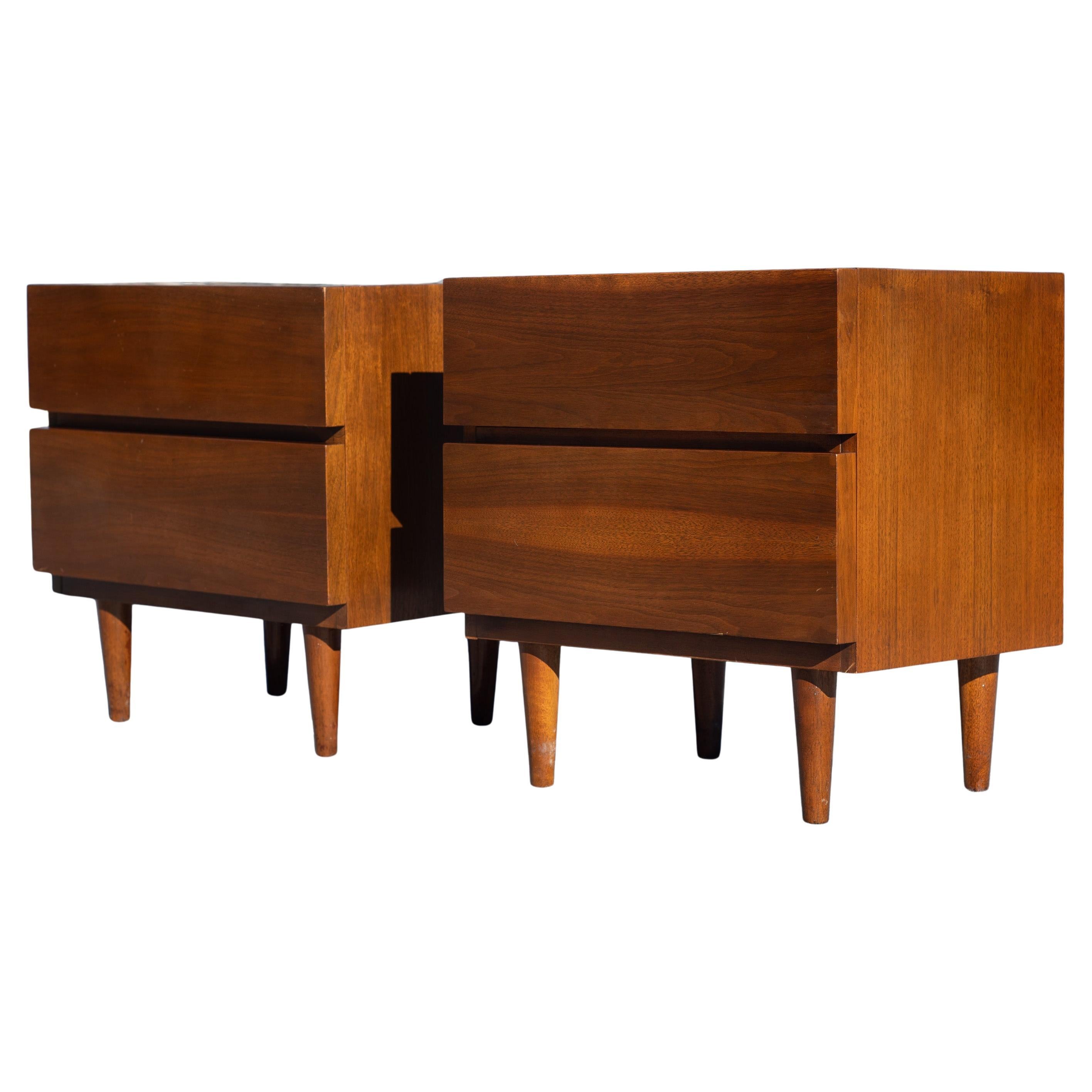 Probablement conçue par Merton Gershun, cette paire de tables de nuit présente un aspect minimaliste, presque brutal, avec un corps rectangulaire et des tiroirs carrés. L'aspect est adouci par les pieds fuselés. Chaque table de nuit possède deux