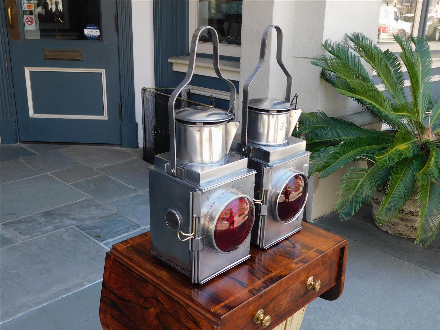 Pair of American polished steel railroad Signal lanterns with flanking hinged doors, scrolled carrying handles, vented tops, rear mounting brackets, and the original Fresnel circular red lenses. Originally oil and can be electrified if desired. Late