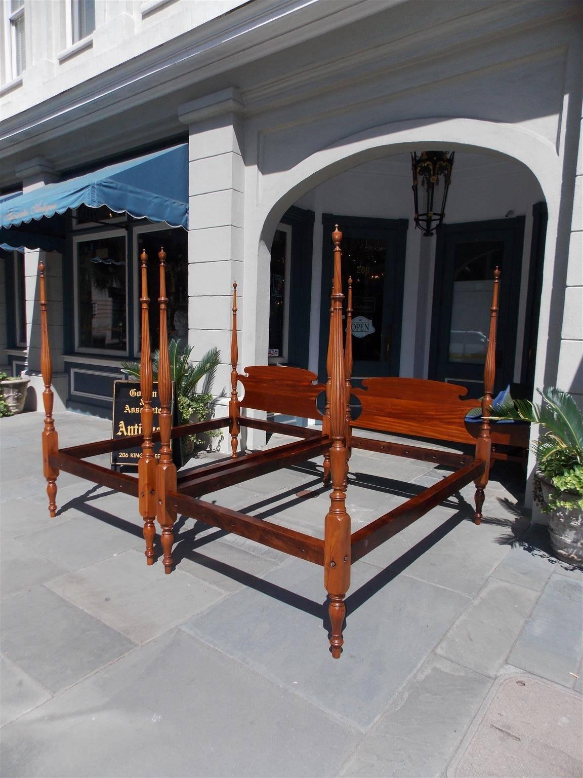 Pair of American Sheraton mahogany four-poster twin beds with carved scrolled headboards, bulbous reeded post, flanking urn finials, pine side rails, and terminating on the original blocked bulbous ringed legs, Early 19th century.


 