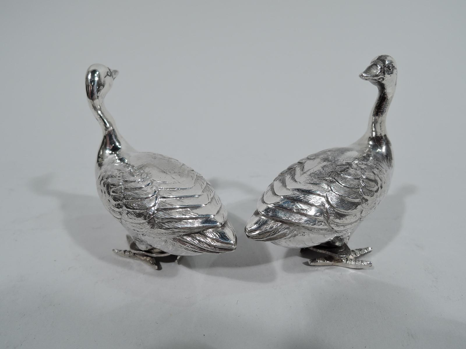 Pair of American sterling silver figural salt and pepper shakers, circa 1920. Each: A waddling goose with imbricated feathers and elongated neck. Scaly talons mounted to threaded cover. Breast pierced. One bird looks to the side, the other looks